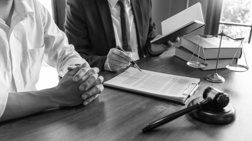 Two people in suits discussing documents at a desk with books and a magnifying glass - ev law in Bundall, QLD
