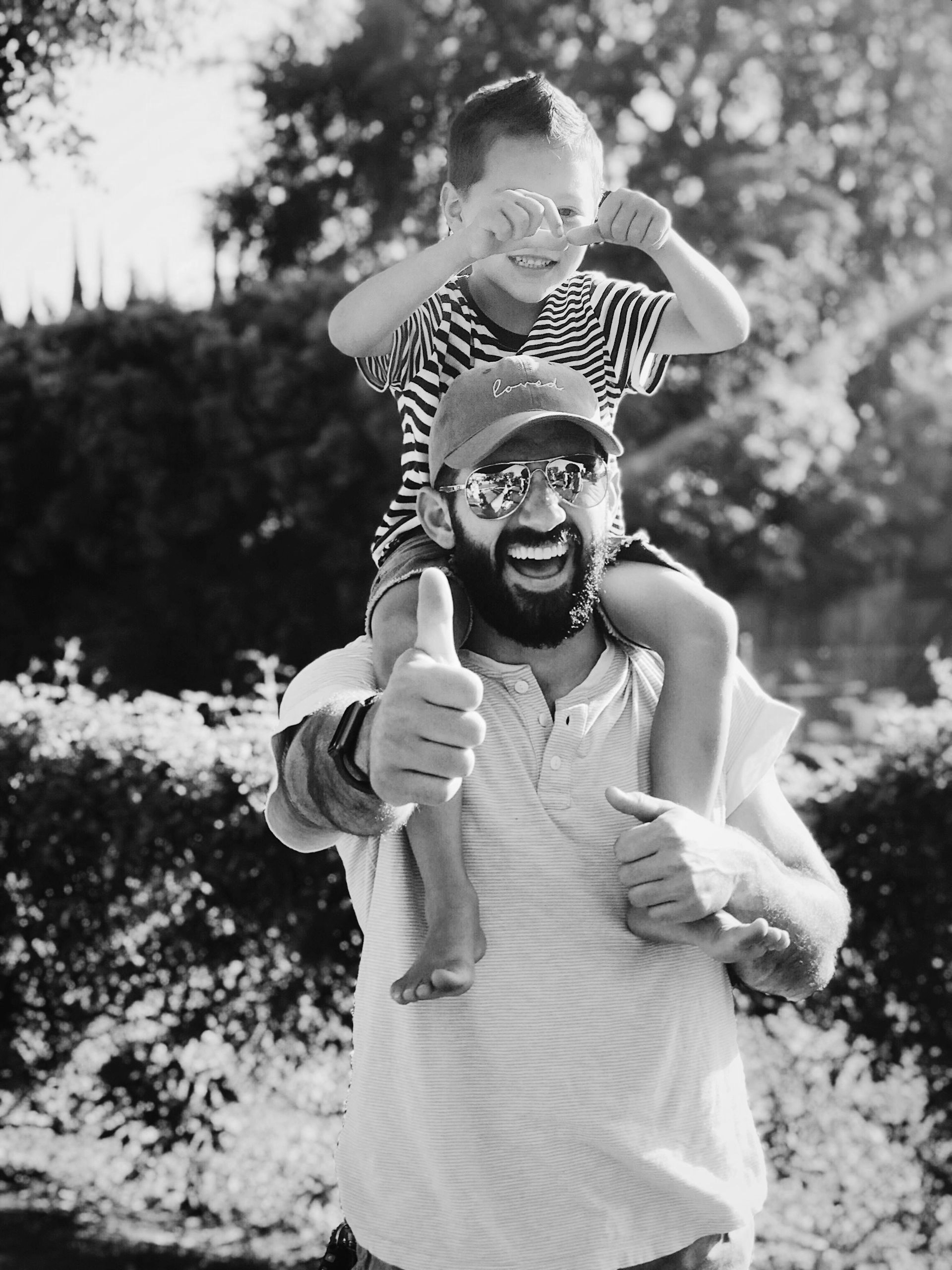 Smiling man carrying a child on his shoulders outdoors in a sunny park - ev law in Bundall, QLD