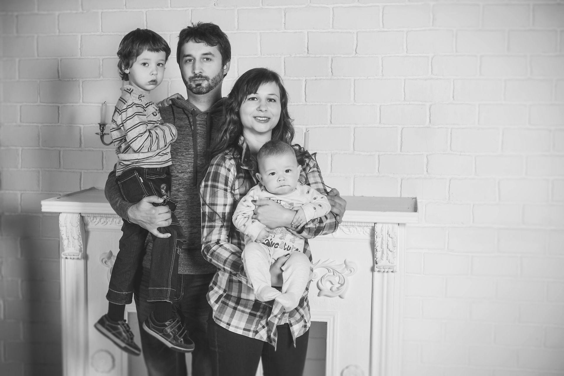 Family of four posing indoors by a mantel, with a man holding a child and a woman holding a baby. - ev law in Bundall, QLD