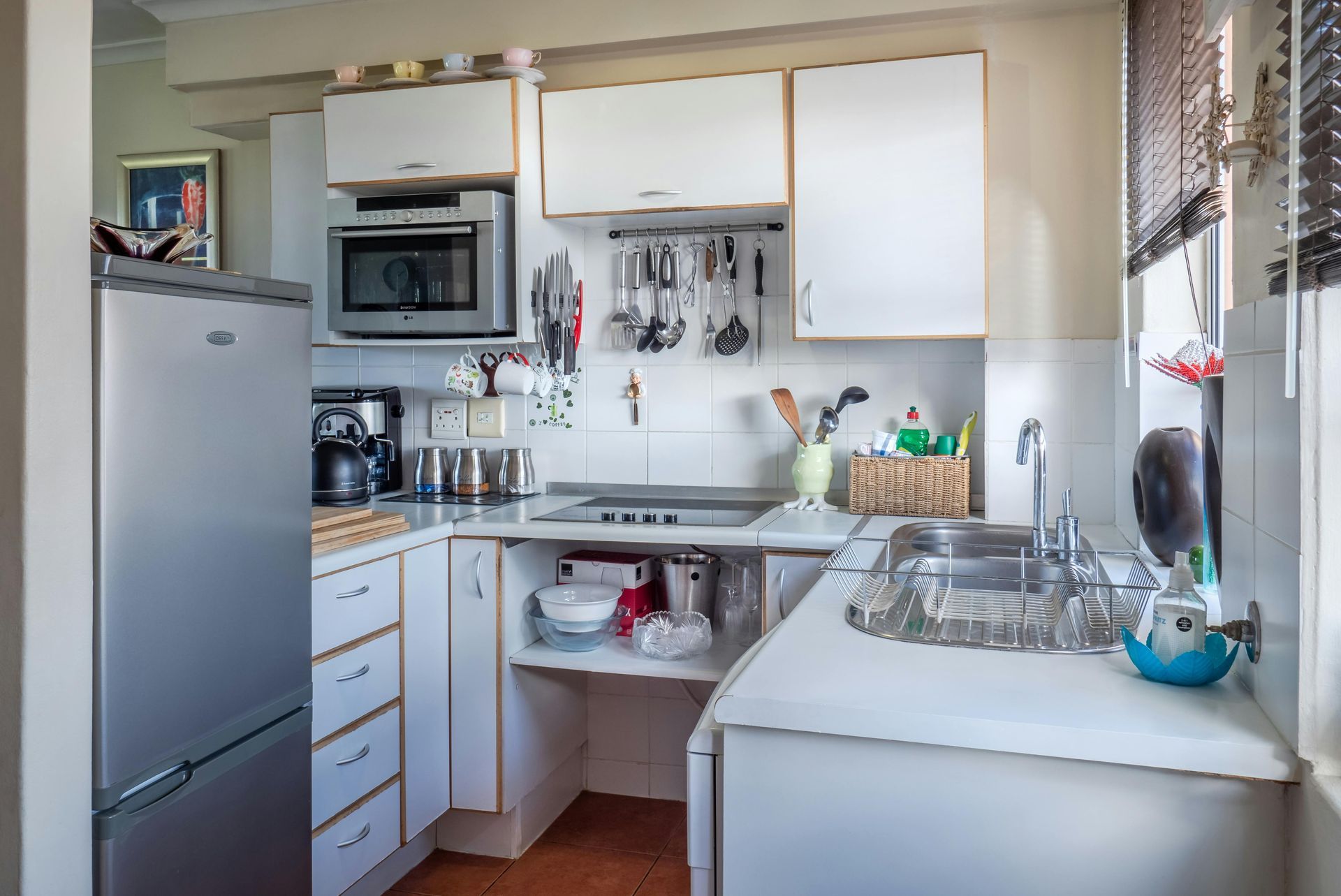 Small white kitchen with appliances, cabinets, and sink; a window with blinds.