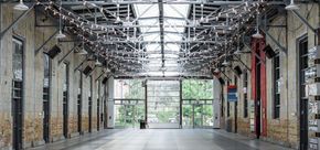 Interior of a large warehouse space with glass doors at the far end, showing outdoor greenery.