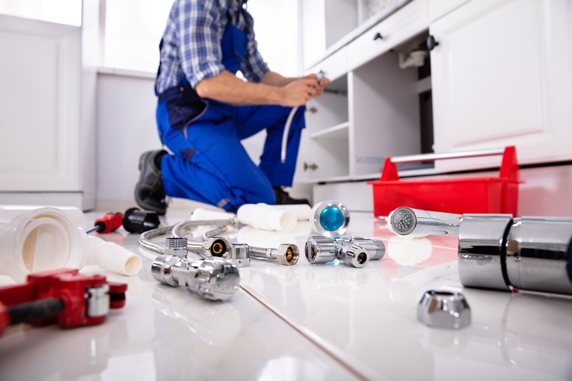 Plumber kneeling in front of a cabinet, working on pipes and surrounded by plumbing tools.