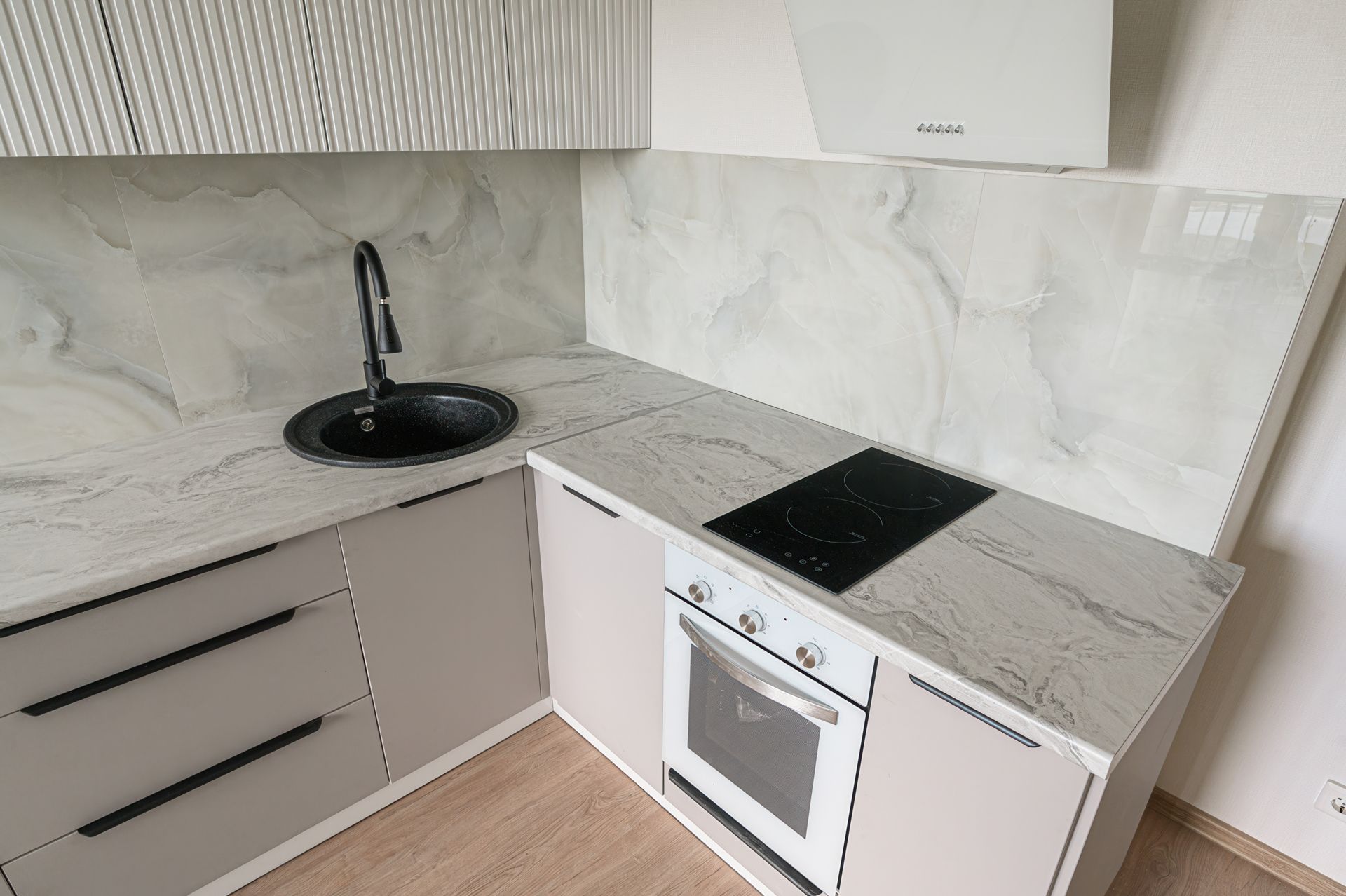 Kitchen with gray cabinets, marble-look countertops, black sink and cooktop, and white range hood.