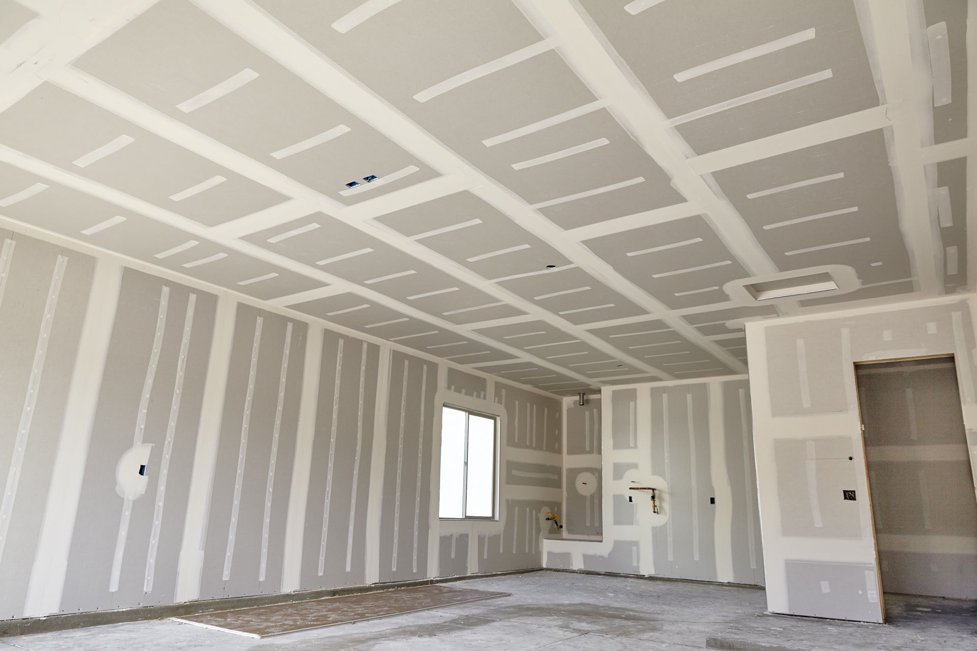 Interior of a room under construction with exposed drywall on the walls and ceiling.