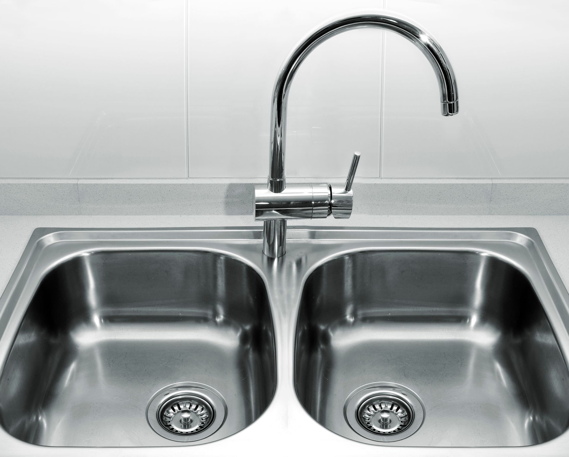 A stainless steel double-basin kitchen sink with a chrome gooseneck faucet centered against a white tiled backsplash.