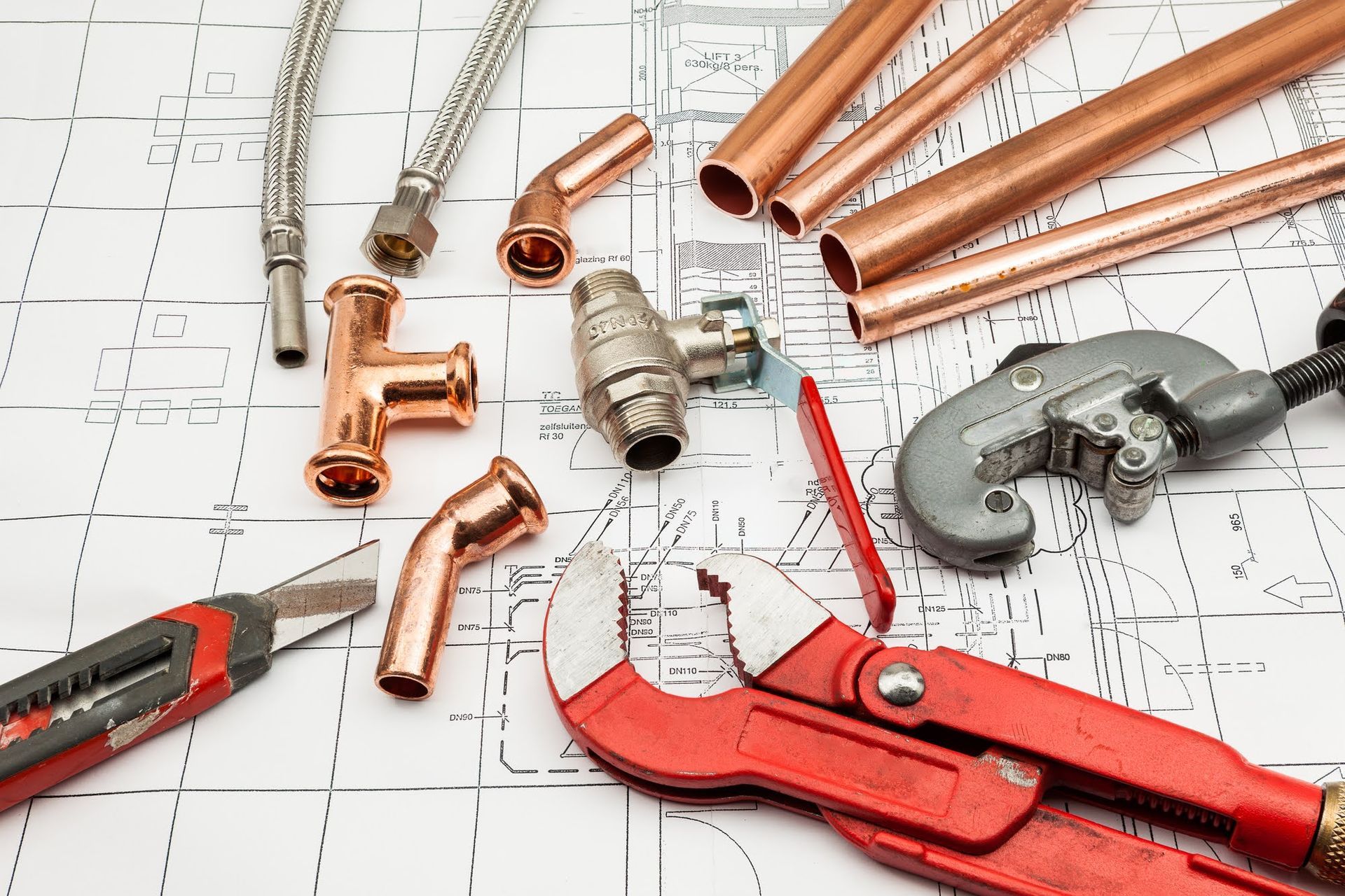 Copper pipes, fittings, a ball valve, and plumbing tools, including a pipe cutter and wrench, laid over a floor plan.