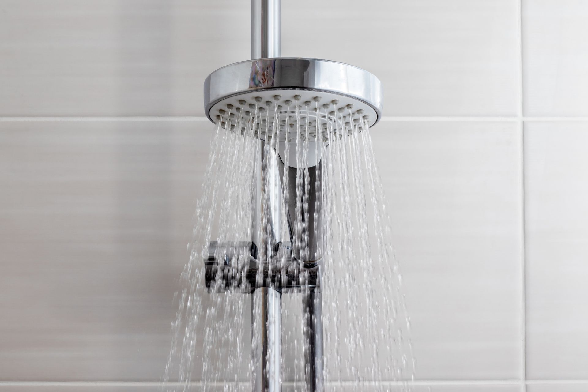 A chrome shower head mounted on a white tiled wall, with water spraying downward.