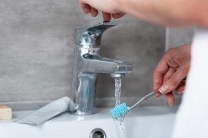 Woman Wetting Toothbrush in Sink — Lisle, IL – Jim Dhamer Plumbing and Sewer, Inc. Woman Wetting Toothbrush in Sink — Lisle, IL – Jim Dhamer Plumbing and Sewer, Inc.