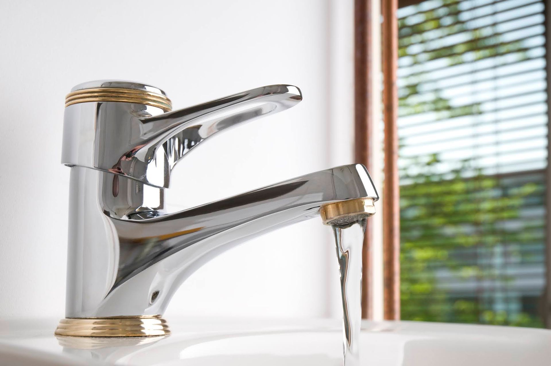A chrome bathroom faucet with gold accents flowing with a steady stream of water into a white sink.