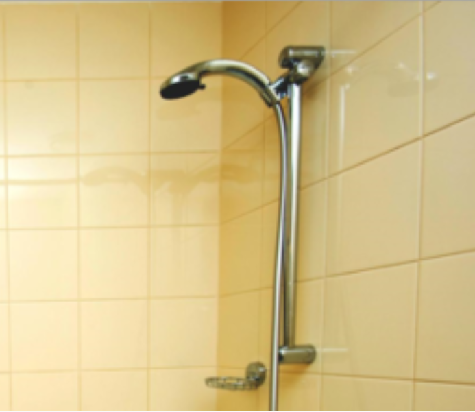 Silver showerhead and bar against beige tiled wall.