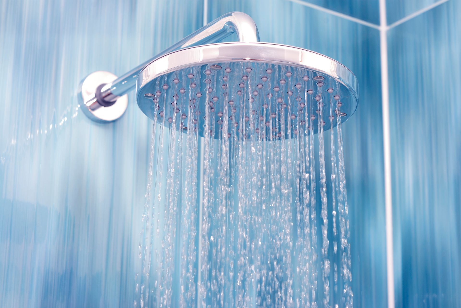 A circular chrome shower head mounted on a blue tiled wall, raining water downward.