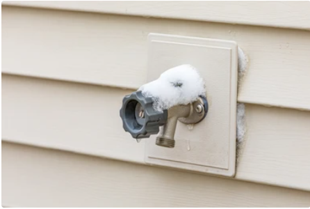 An outdoor water spigot covered in snow and ice, mounted on beige siding.