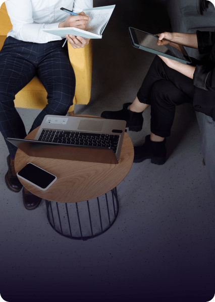 People seated around a small table, working with a laptop, tablet, and notepad in a modern setting.