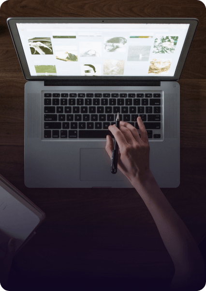 Person using laptop with pen, browsing website, dimly lit setting.