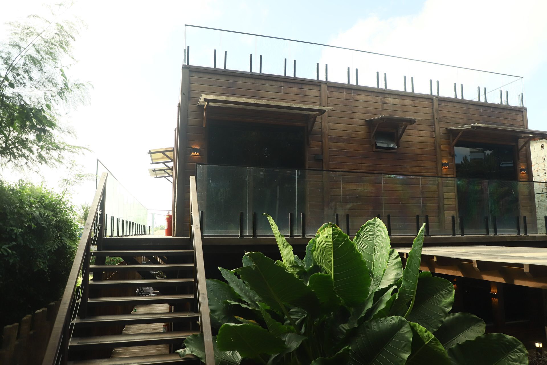 Casa moderna de tijolos com escada, varanda e vegetação exuberante na frente.