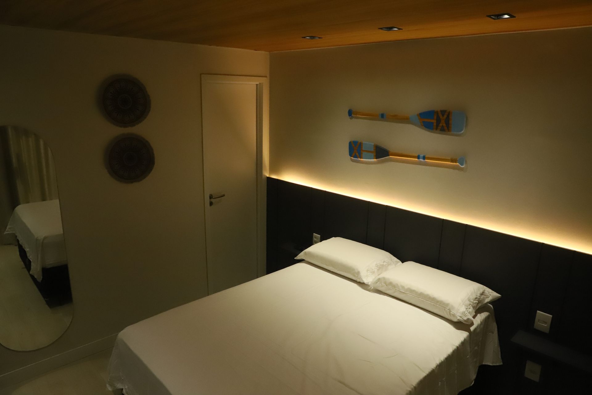 Quarto moderno com cama, obras de arte na parede e iluminação ambiente suave.