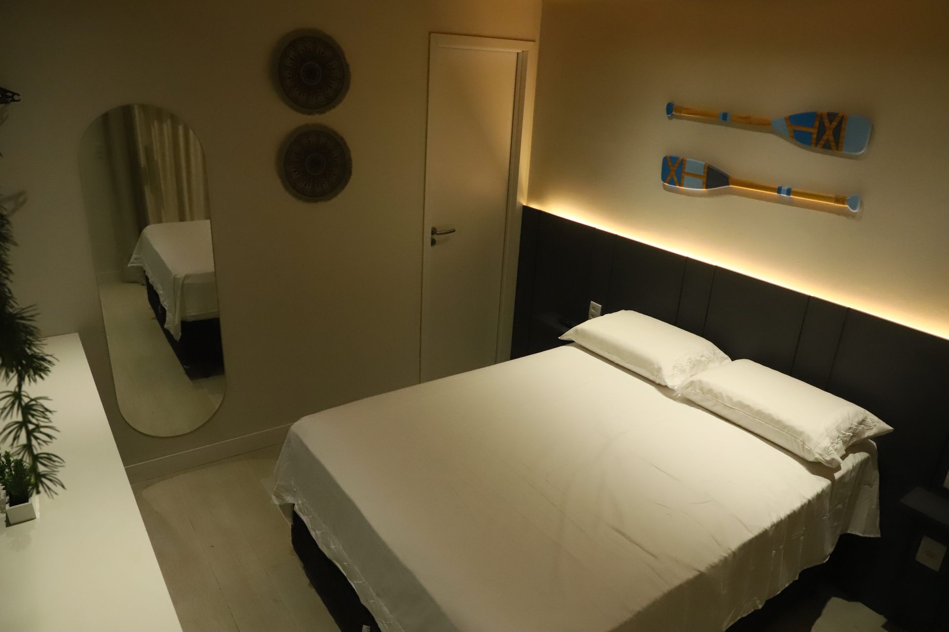 Quarto minimalista com cama de casal, espelho de parede, decoração com tema de skate e iluminação suave.