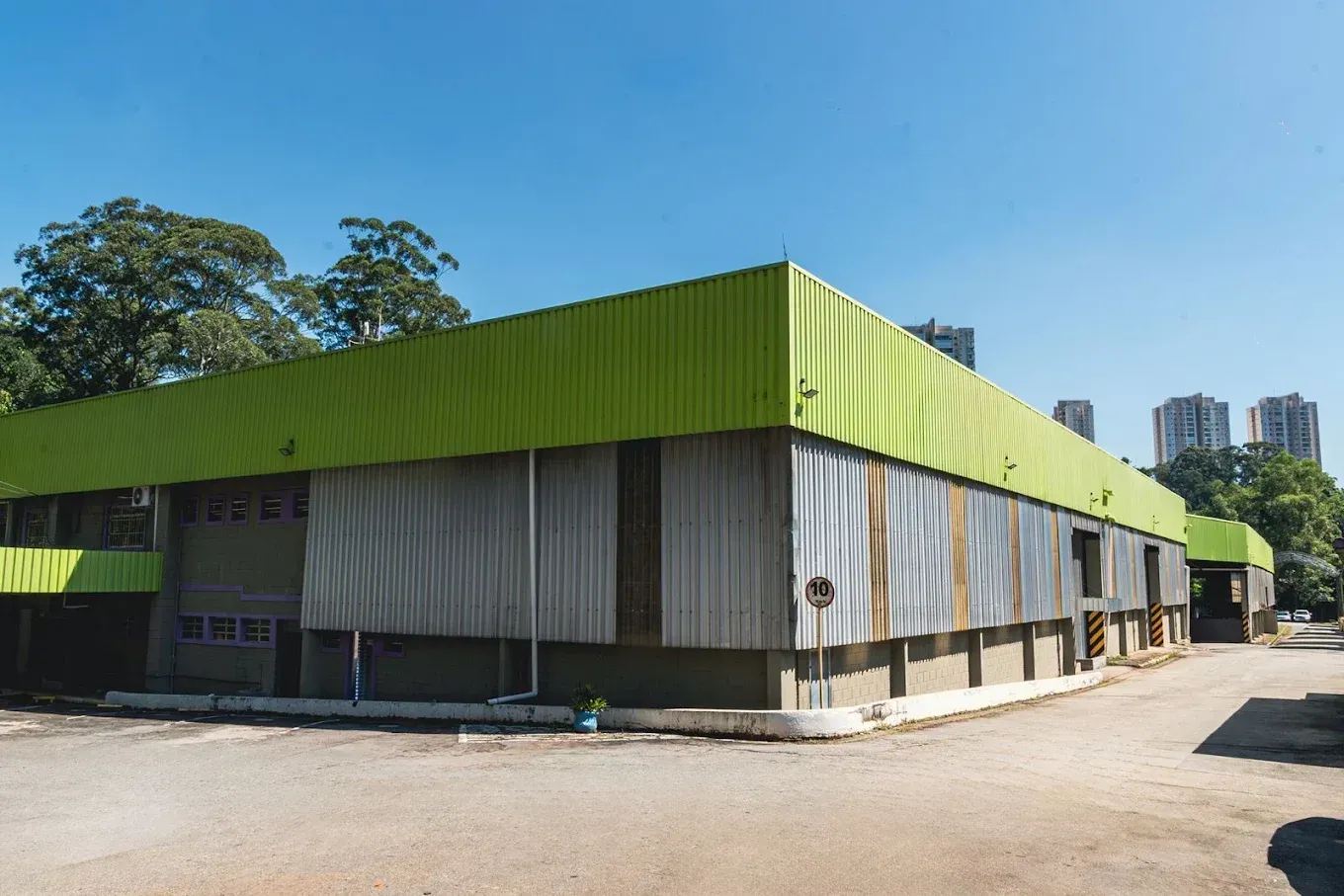 Prédio industrial moderno com telhado verde e paredes cinza em um dia ensolarado.