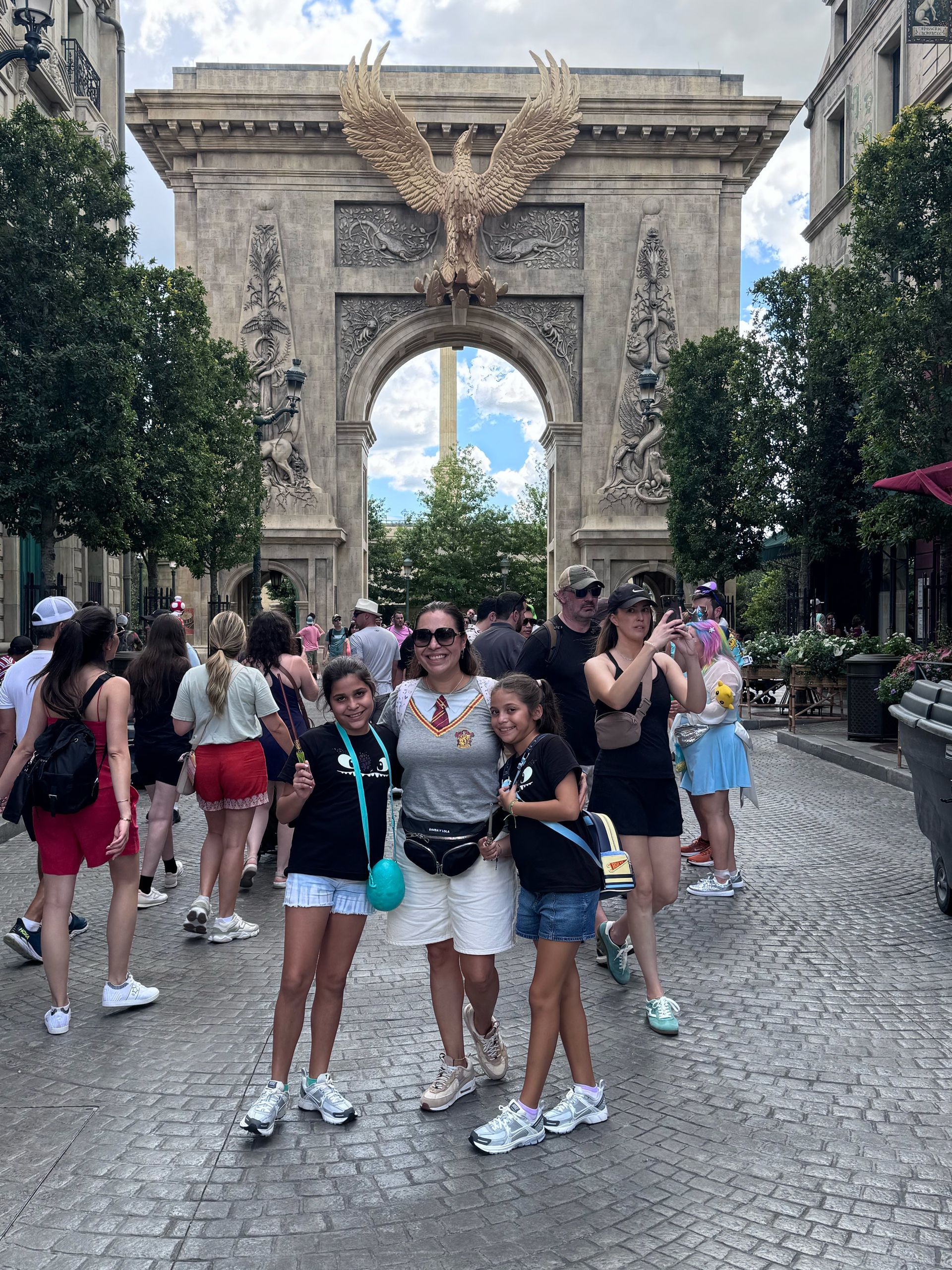 Family posing in front of a stone arch with a golden eagle. People on cobblestone street, sunny day.