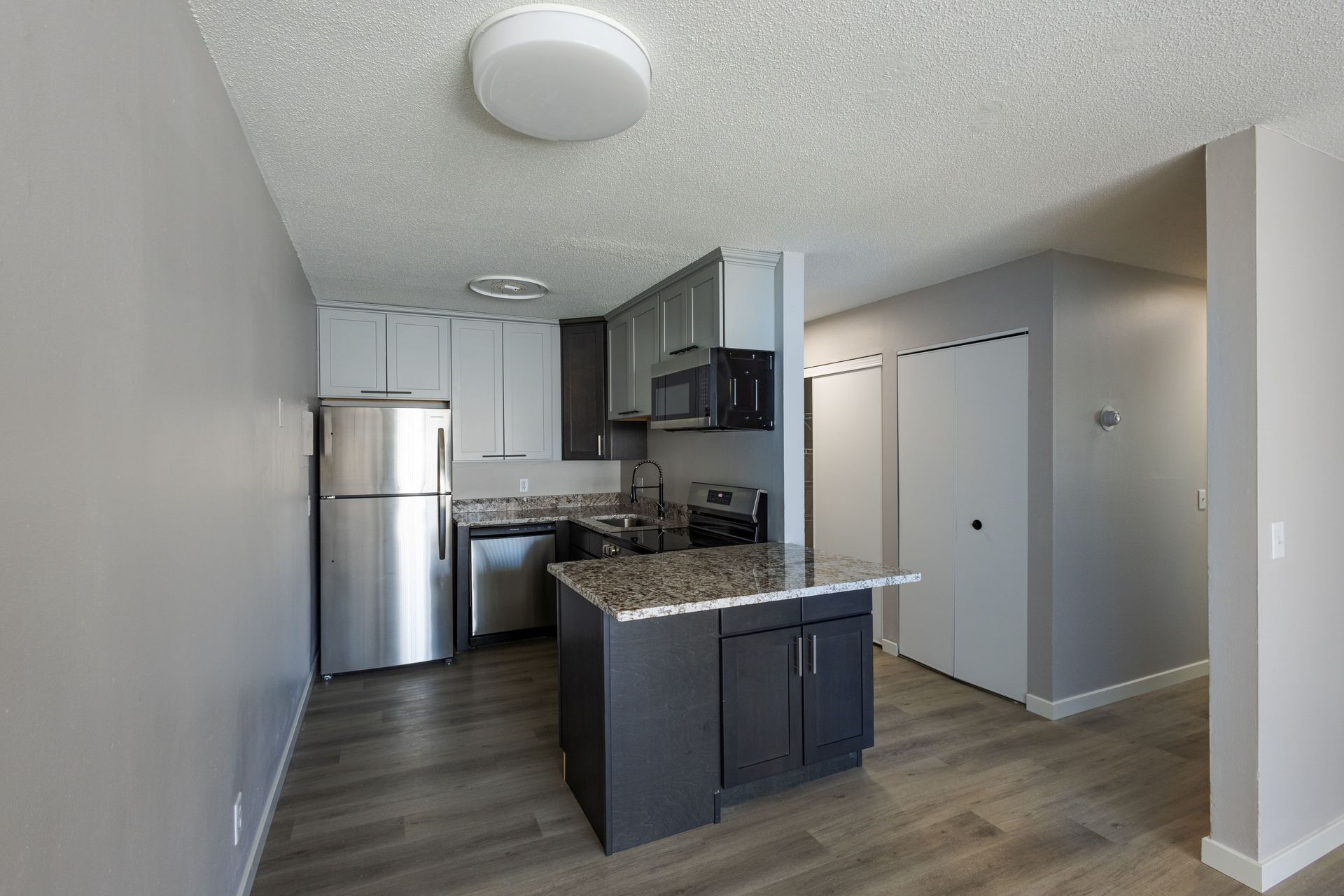 Modern apartment kitchen with stainless steel fridge, dark cabinets, and a small island in an open living space