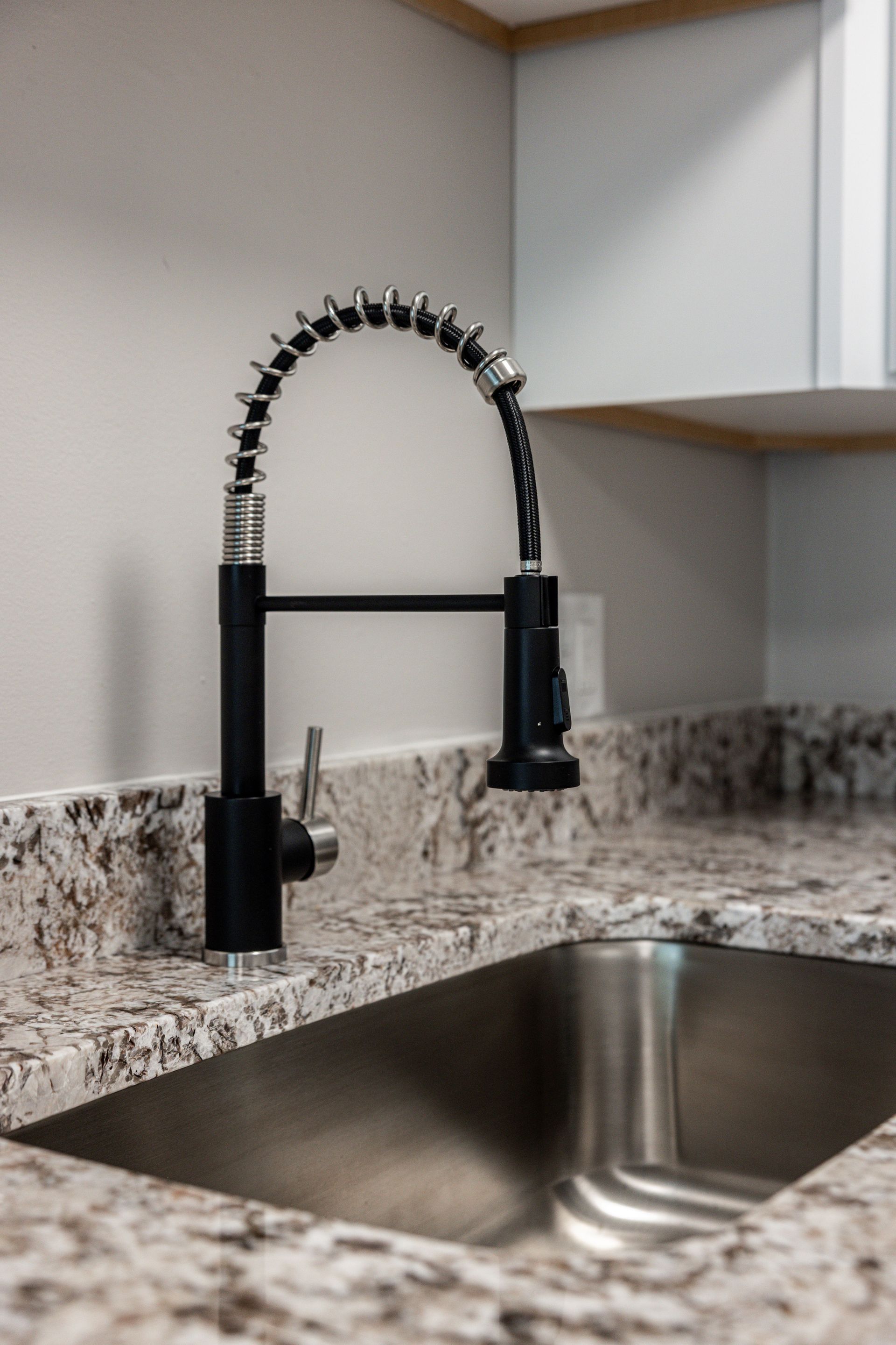 Black pull-down kitchen faucet over a stainless steel sink with a speckled granite countertop
