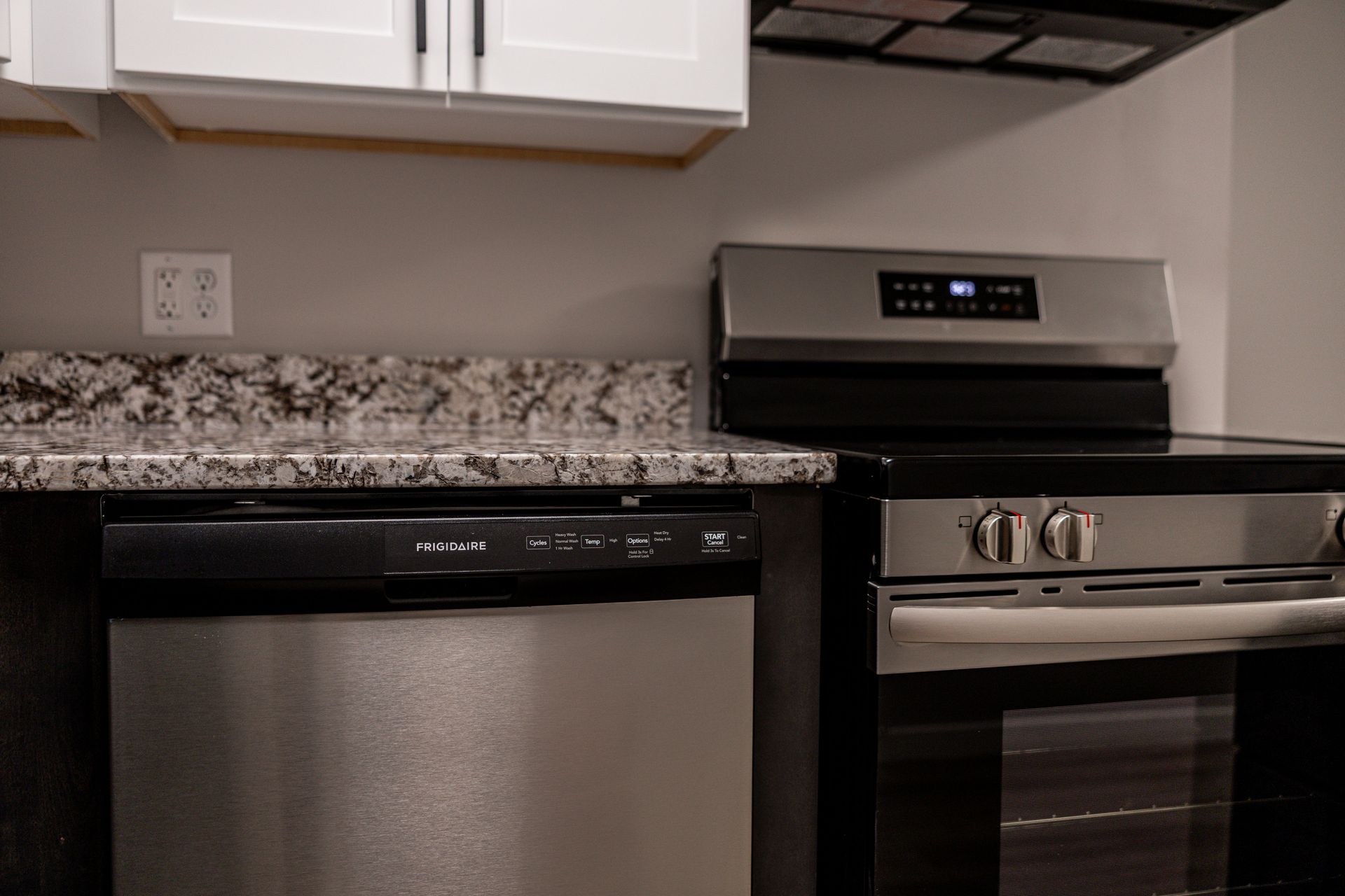 Kitchen with stainless steel dishwasher, stove, and granite countertop under white cabinets