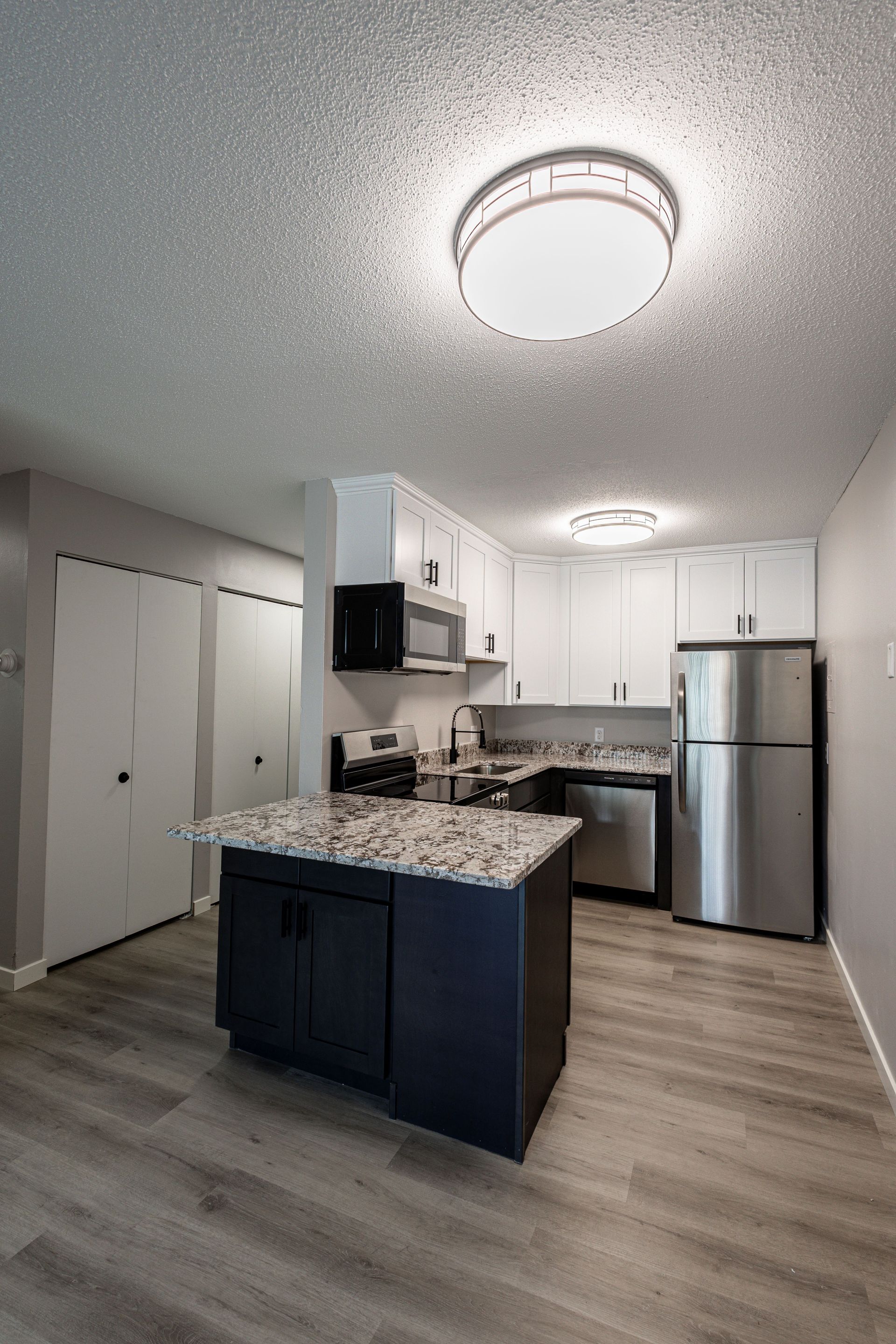 Bright modern kitchen with white cabinets, stainless steel appliances, island, and wood-look flooring.