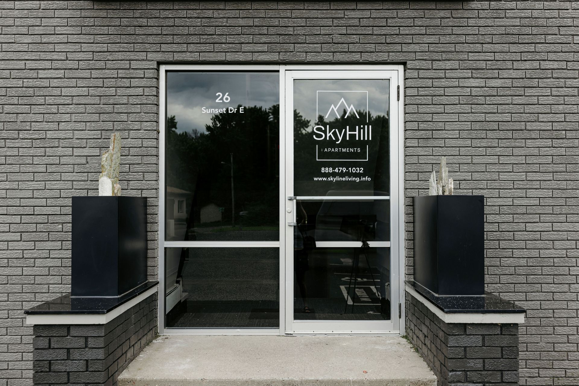 Brick storefront entrance with glass double doors, black planters, and SkyHill signage