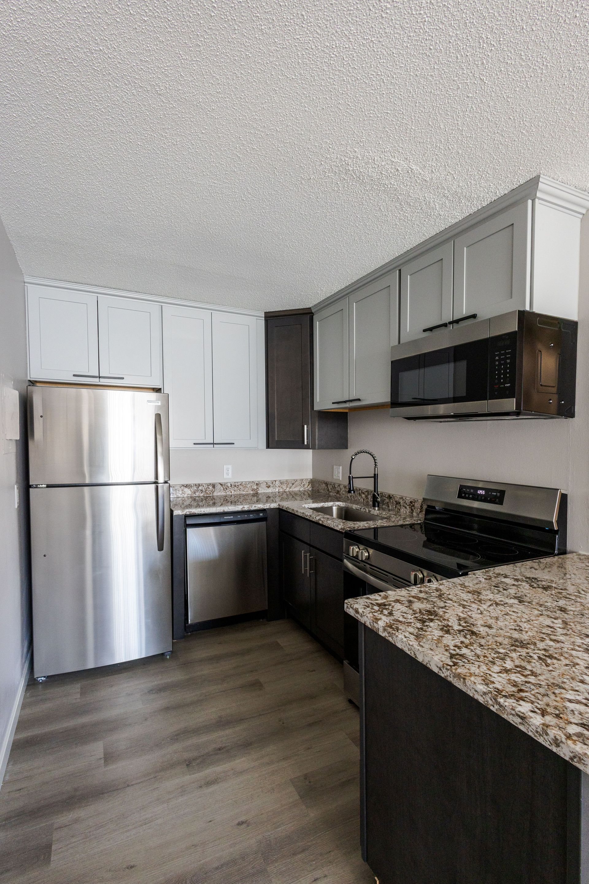 Modern kitchen with stainless steel appliances, gray cabinets, granite countertops, and wood-look flooring