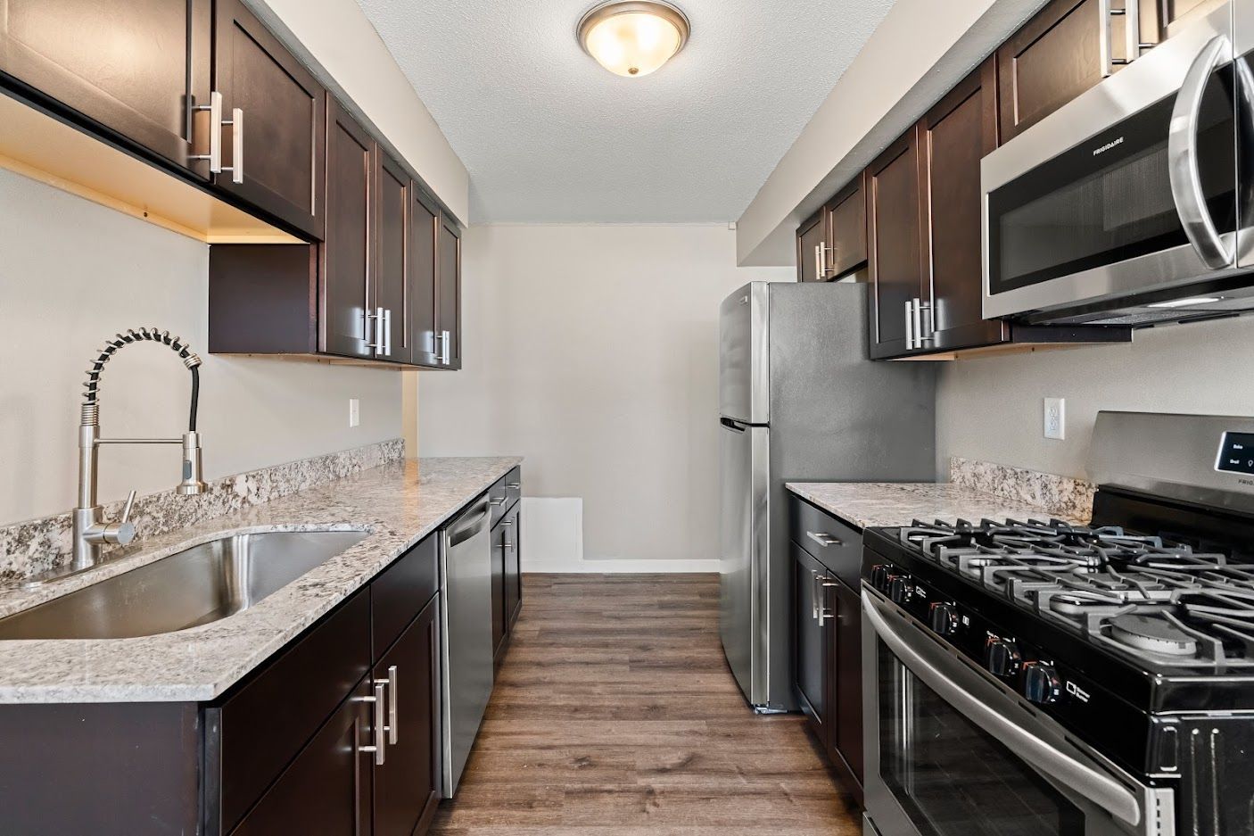 Narrow modern kitchen with dark cabinets, stainless appliances, and granite counters.