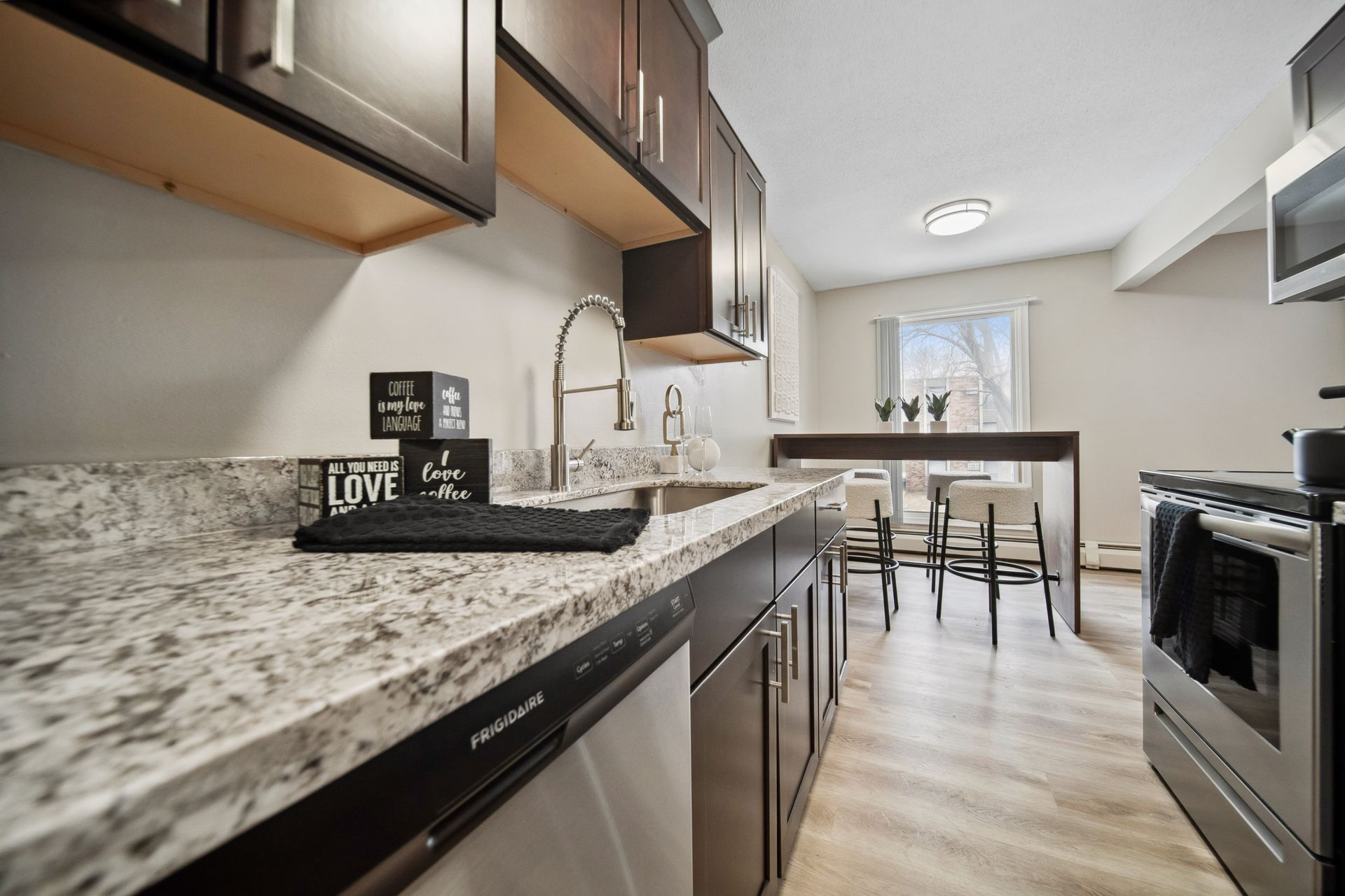 Modern kitchen with granite countertops, stainless appliances, and a small dining table by a bright window
