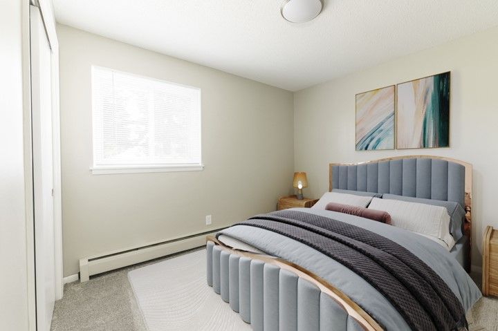 Small bedroom with a gray bed, window blinds, bedside lamp, and abstract wall art.