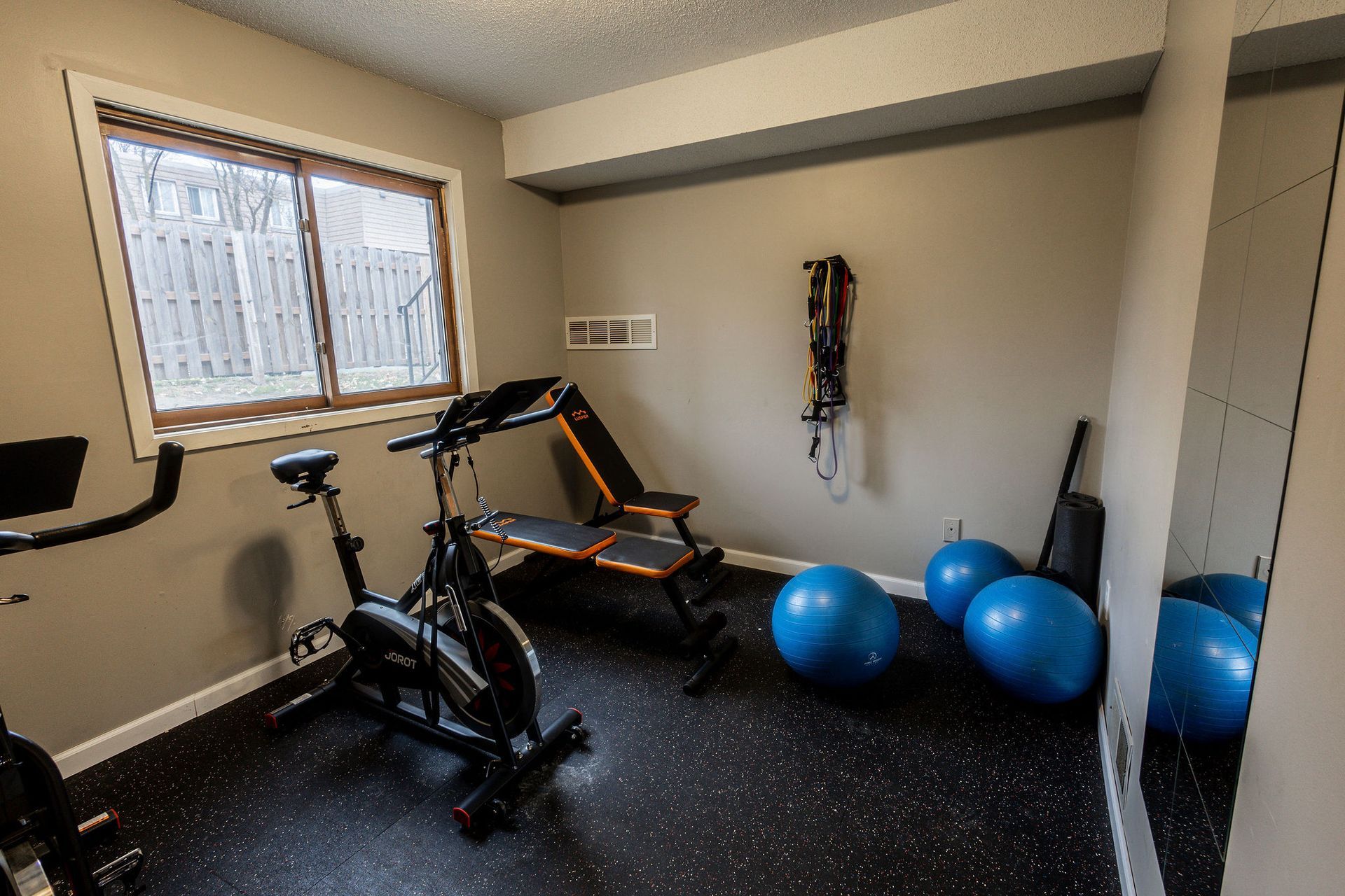 Compact home gym with exercise bike, rowing machine, wall weights, and blue stability balls