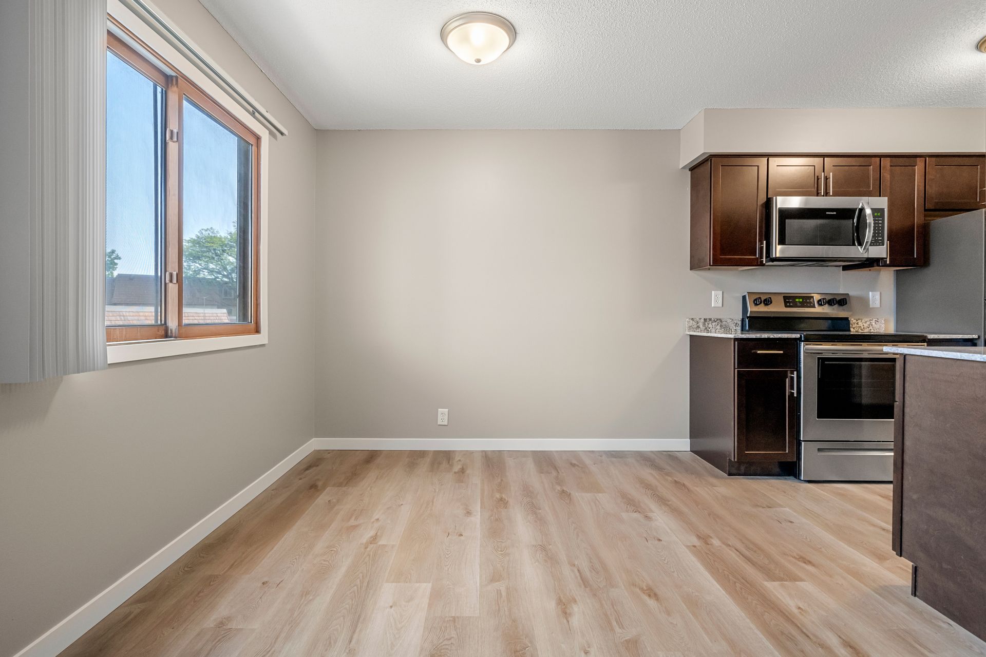 Empty modern kitchen with light wood floors, gray walls, window, and stainless steel appliances