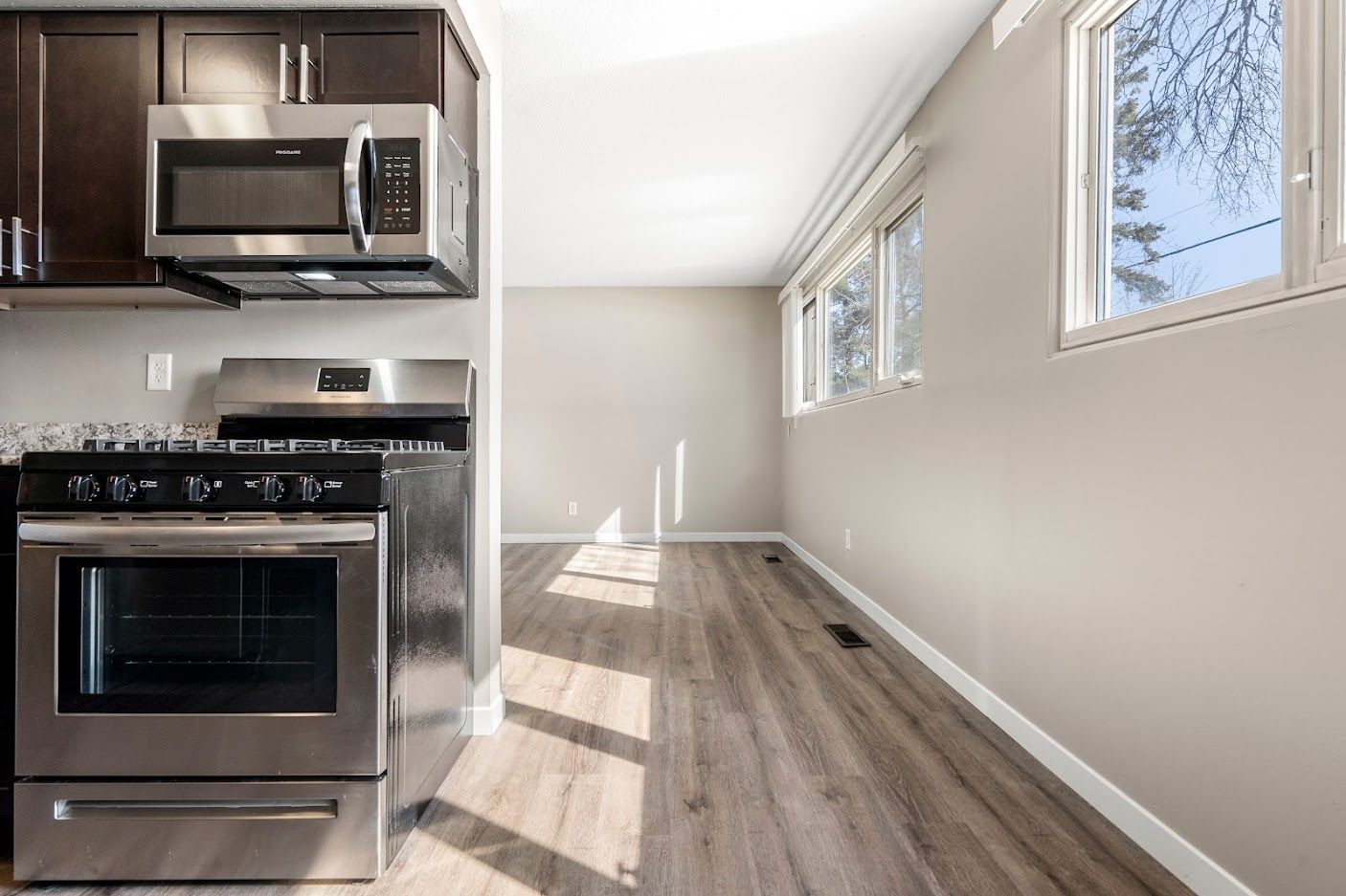 Bright kitchen with stainless steel appliances and a long empty sunlit hallway.