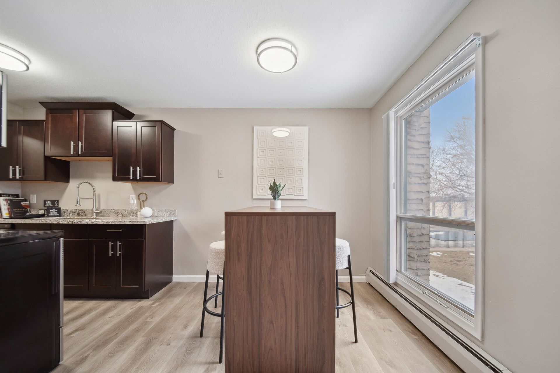 Small kitchen and dining nook with dark cabinets, wood table, and large window.