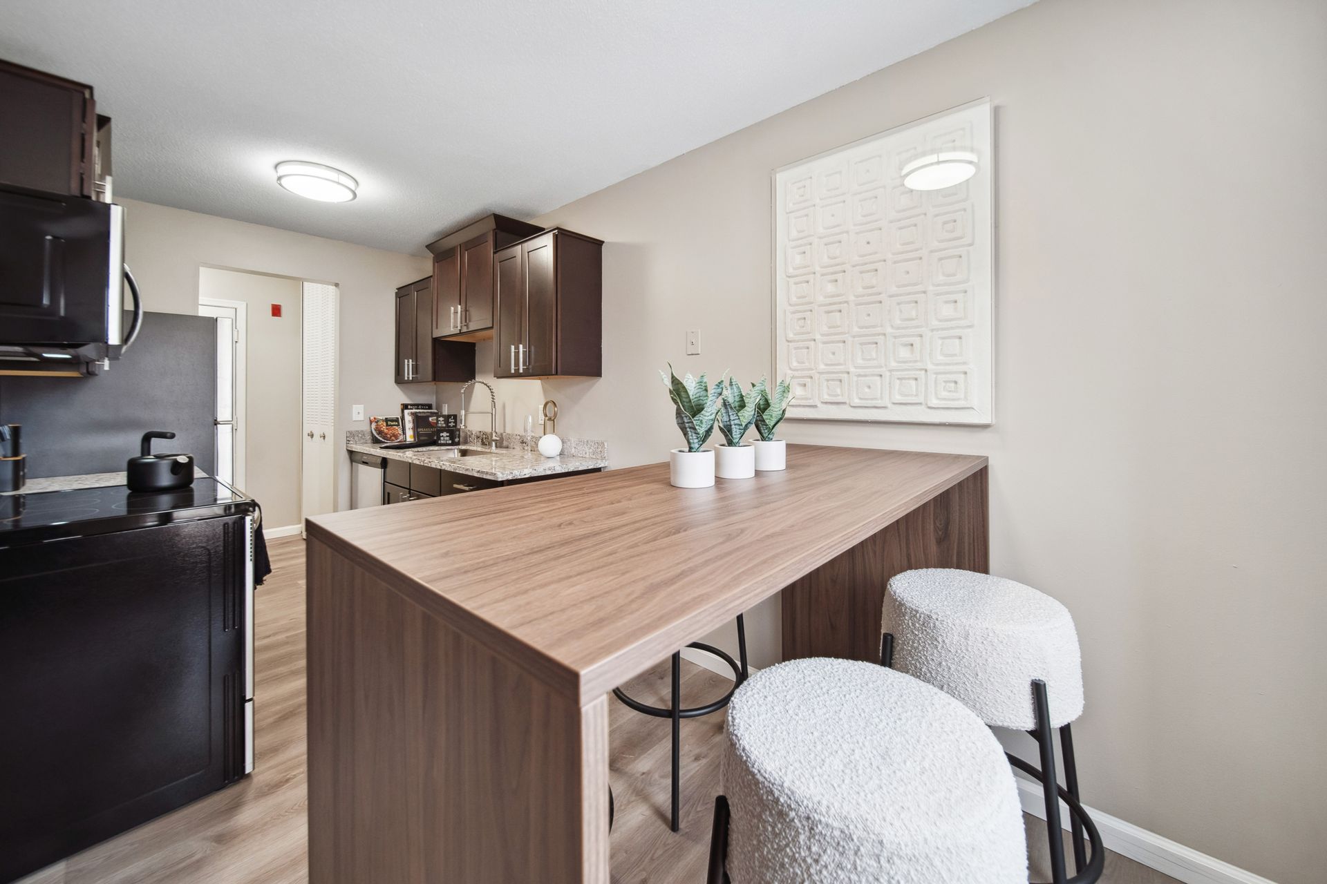 Modern kitchen with a wood breakfast bar, two stools, dark cabinets, and black appliances