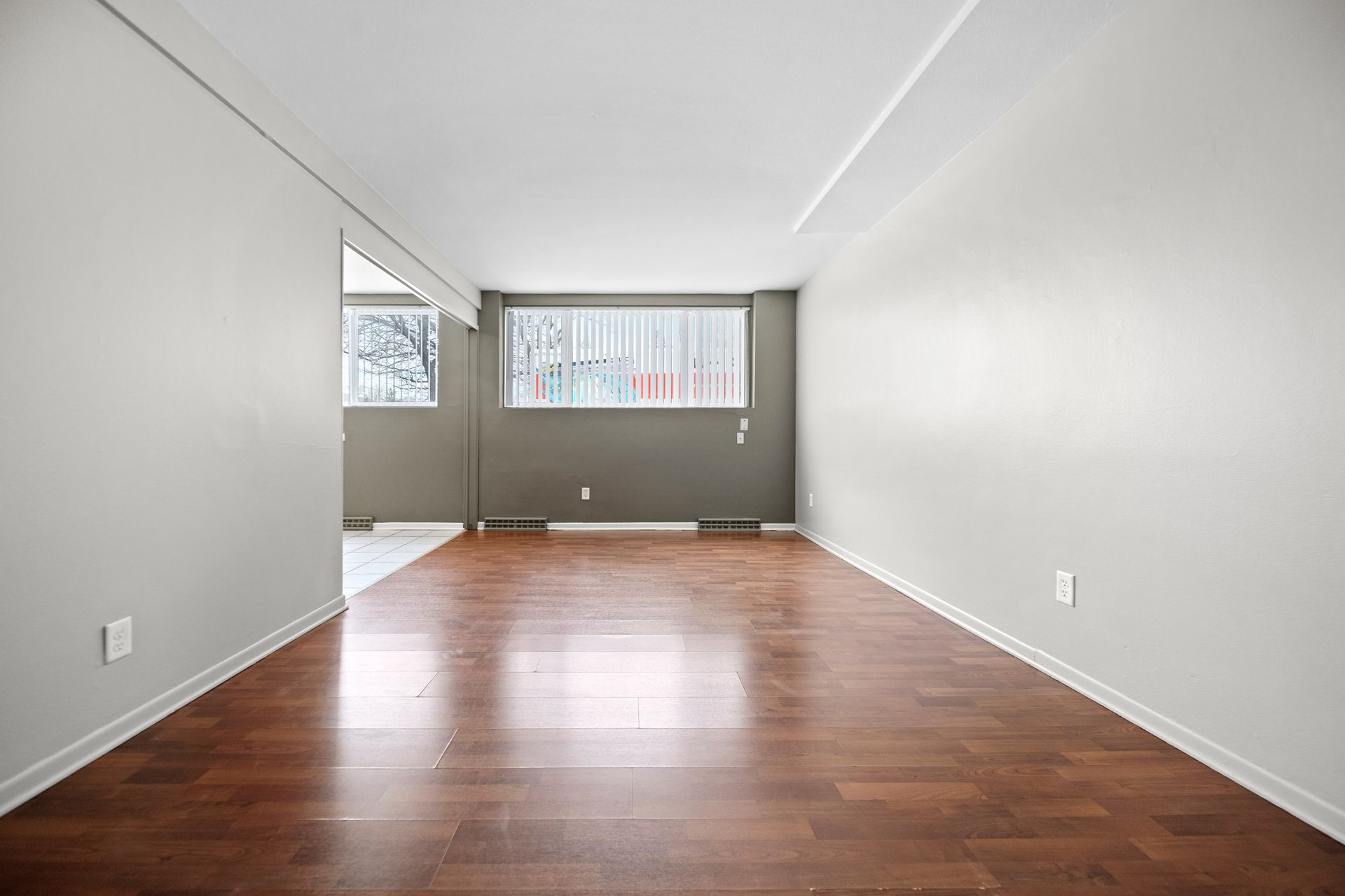 Empty long room with wood floors, white walls, and windows at the far end.