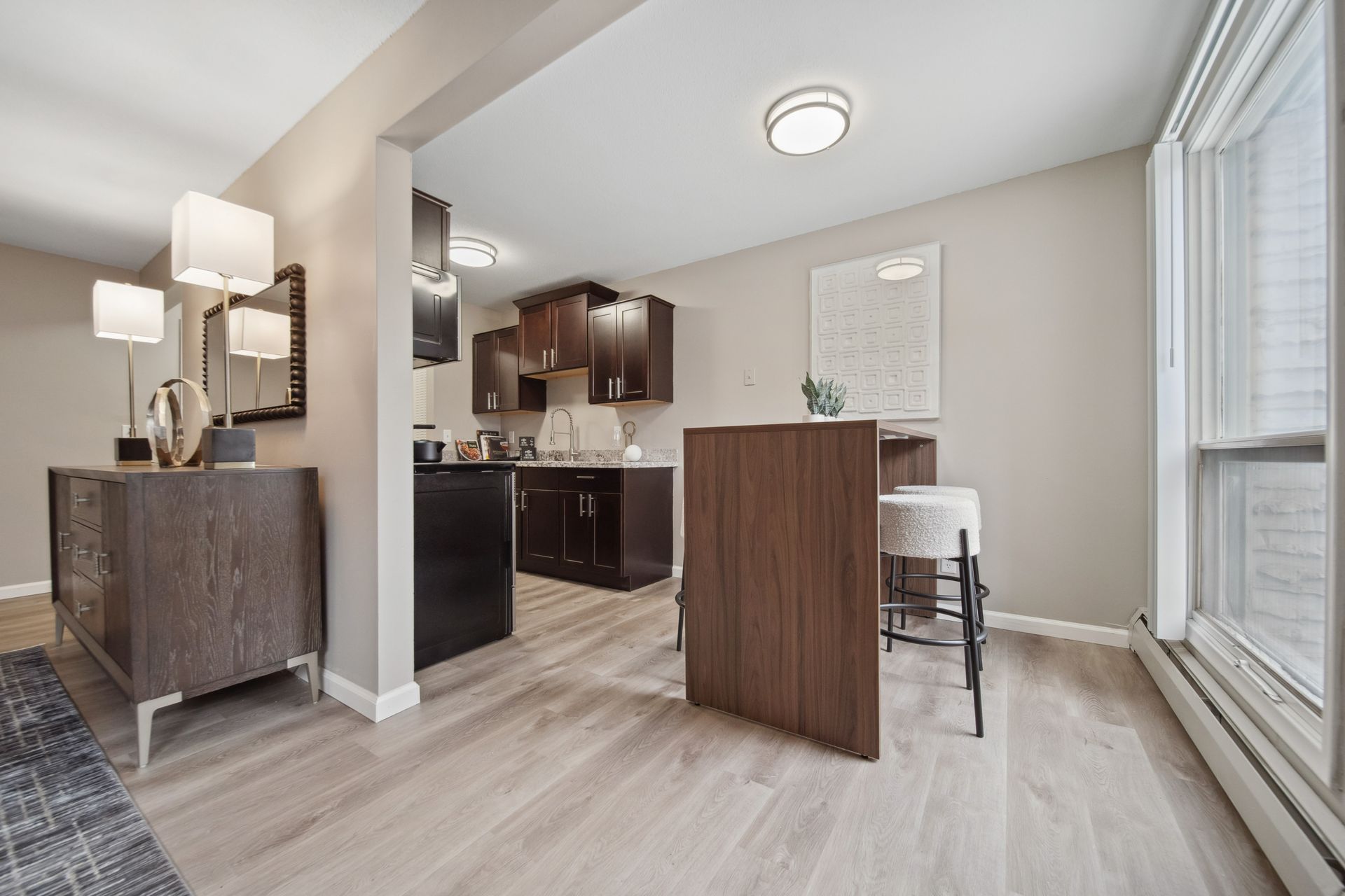 Bright open dining and kitchen area with light wood floors, dark cabinets, and large windows