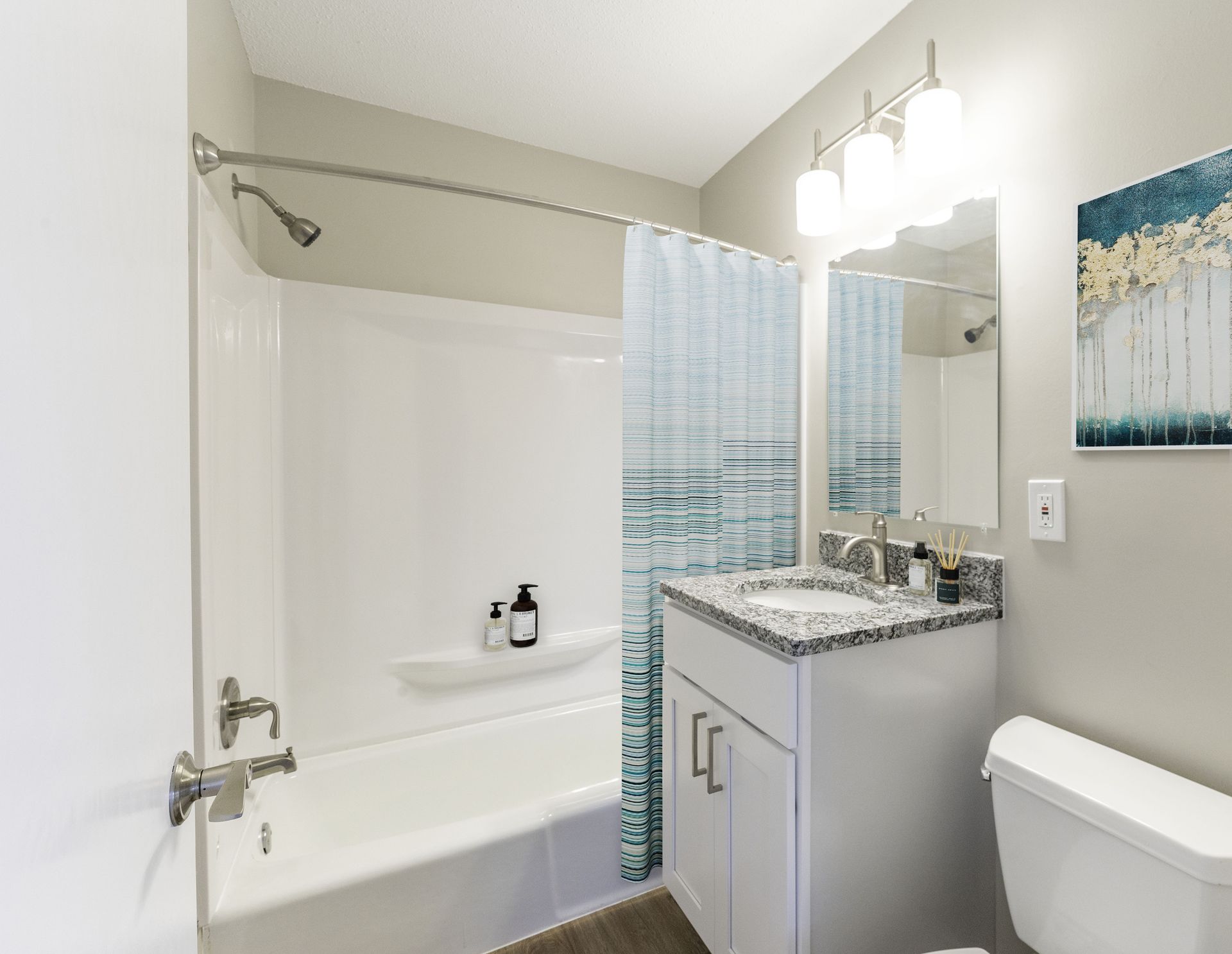 Bright bathroom with white tub, blue mosaic shower curtain, and vanity with lit mirror.