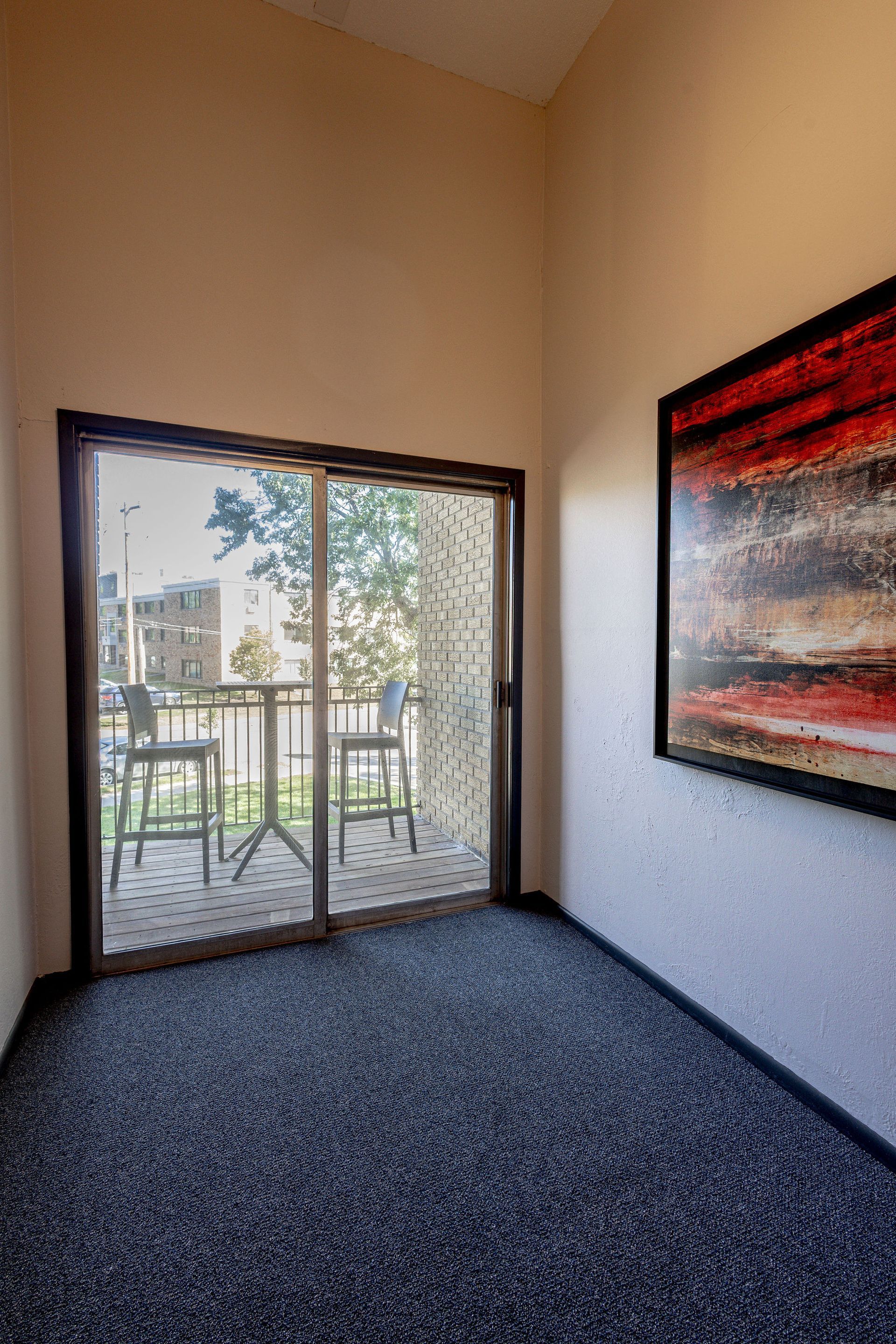 Empty room with dark carpet, sliding glass doors, and a red abstract wall painting.