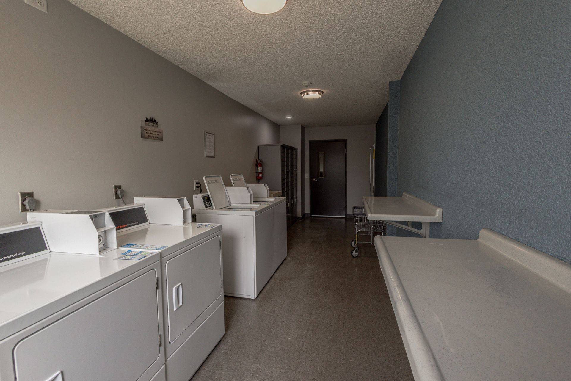 Laundry room with white washers and dryers along a long gray hallway, and a folding table on the right.