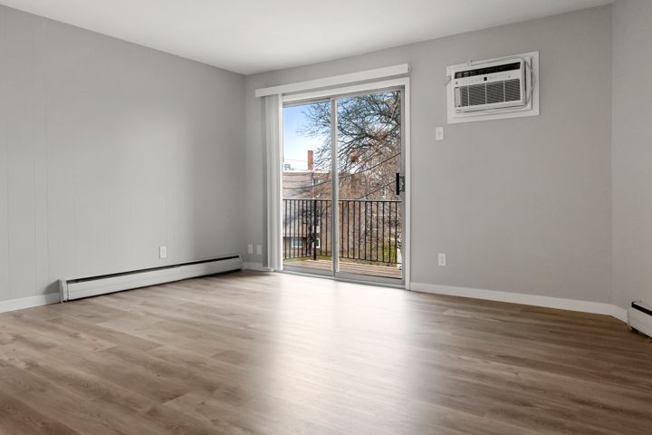 Empty room with light wood floors, gray walls, balcony door, and wall air conditioner