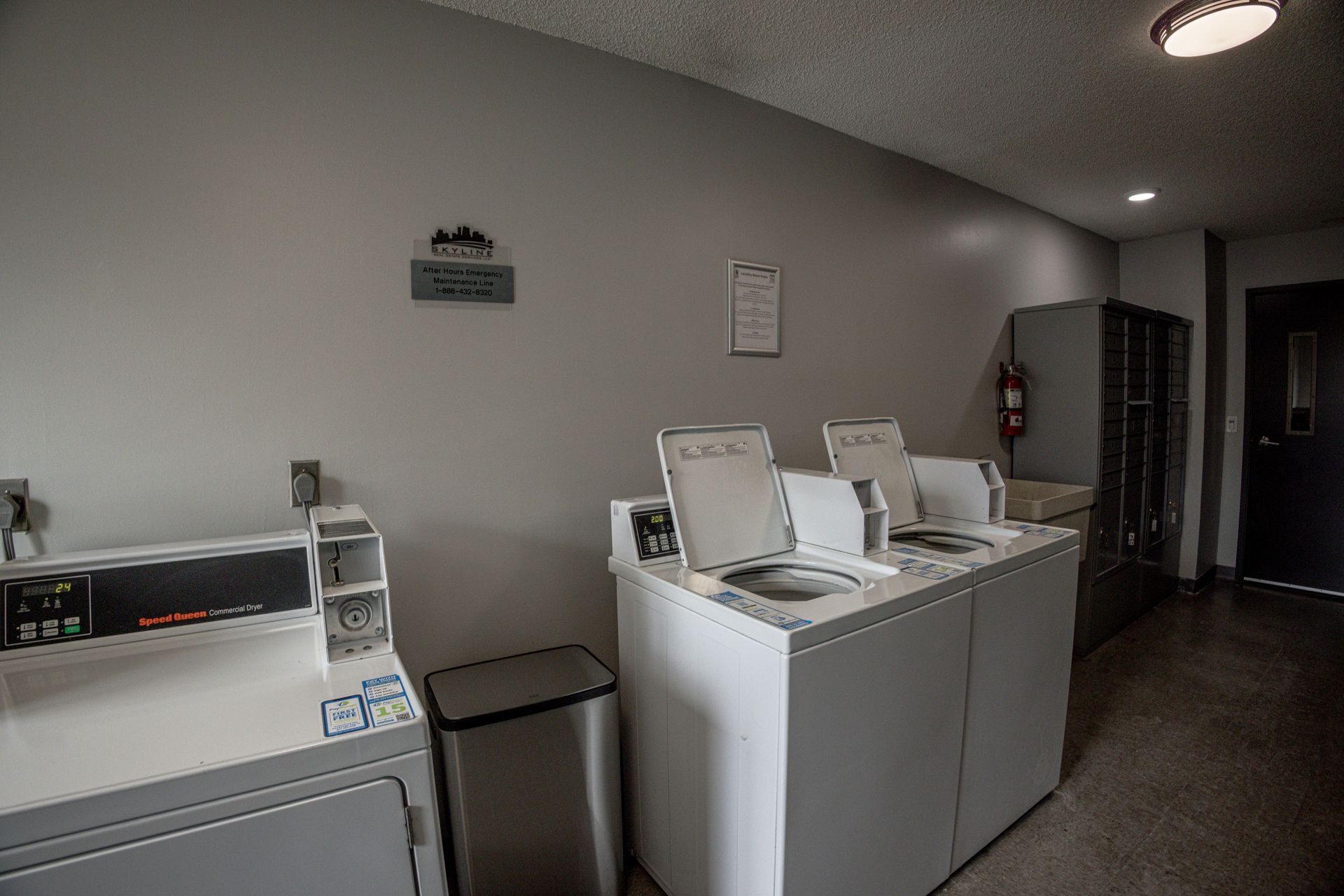 Laundry room with washers, dryers, utility sink, and trash bin in a gray hallway