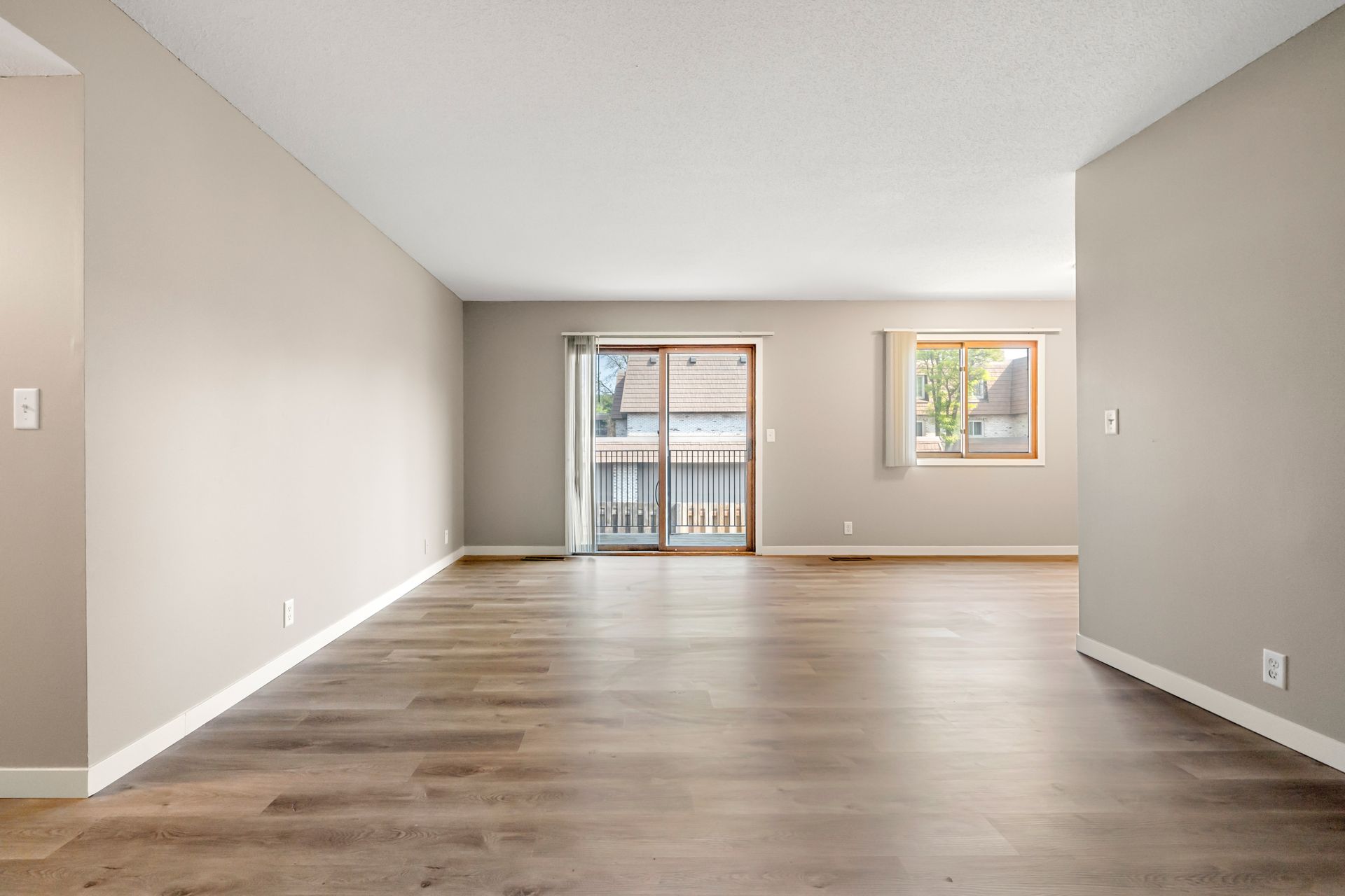 Empty living room with gray walls, wood floor, and sliding glass door to a balcony.