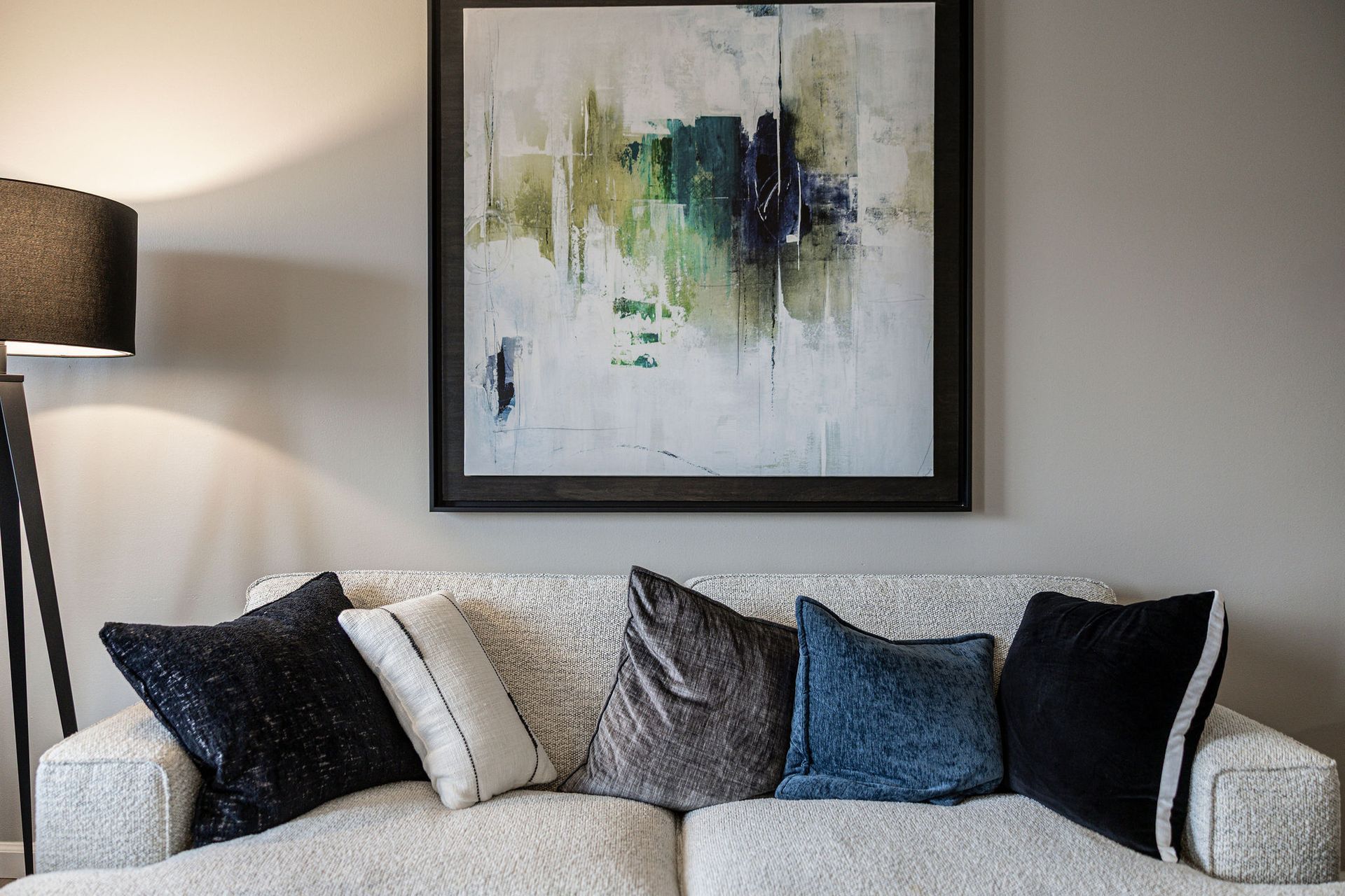 Living room sofa with dark and gray pillows beneath abstract wall art and a floor lamp