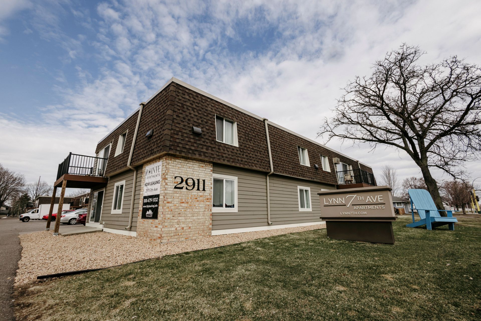 Small beige building with sign “2911,” outdoor stairs, and leafless tree under cloudy sky