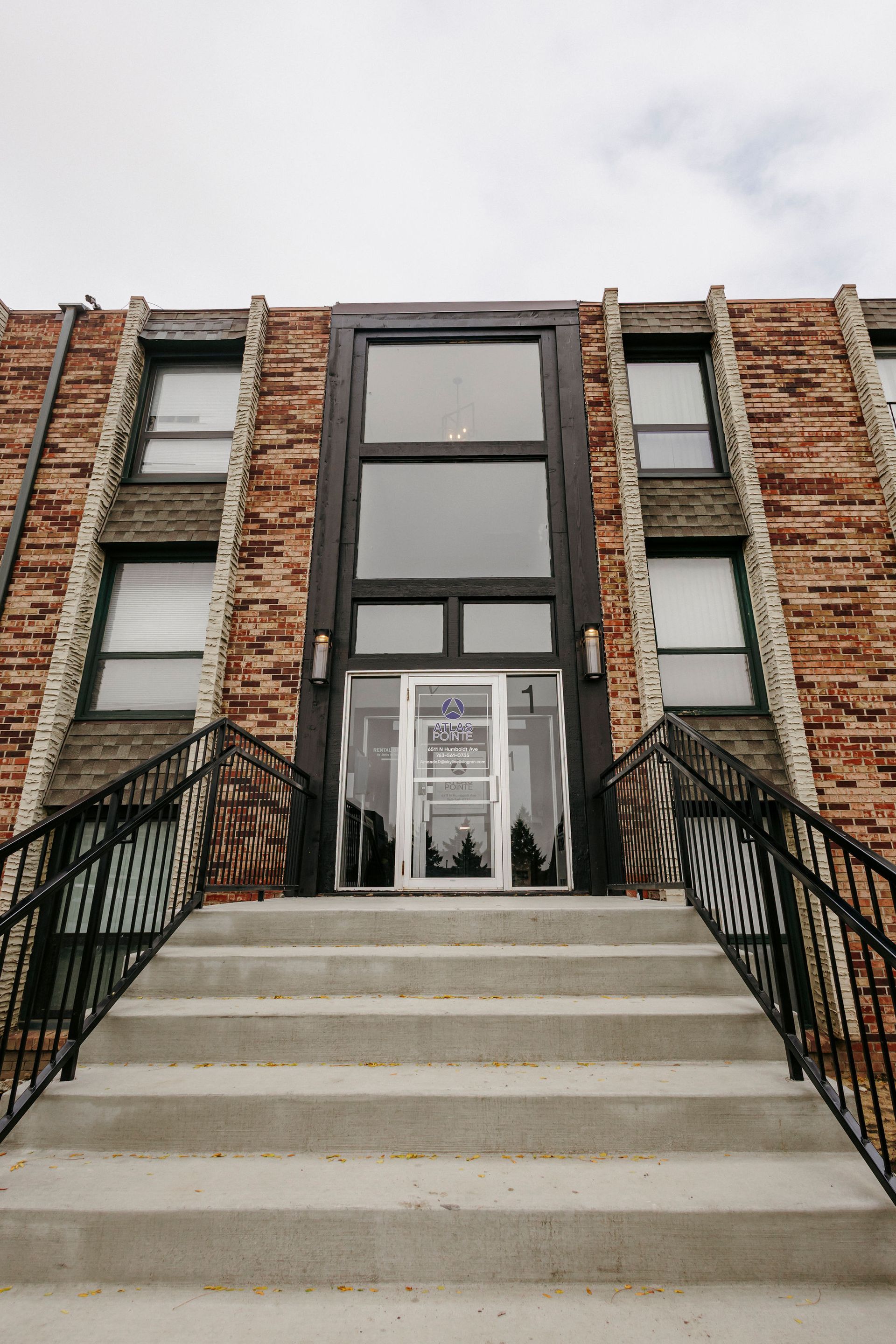 Brick building entrance with black railings and concrete steps leading to glass doors