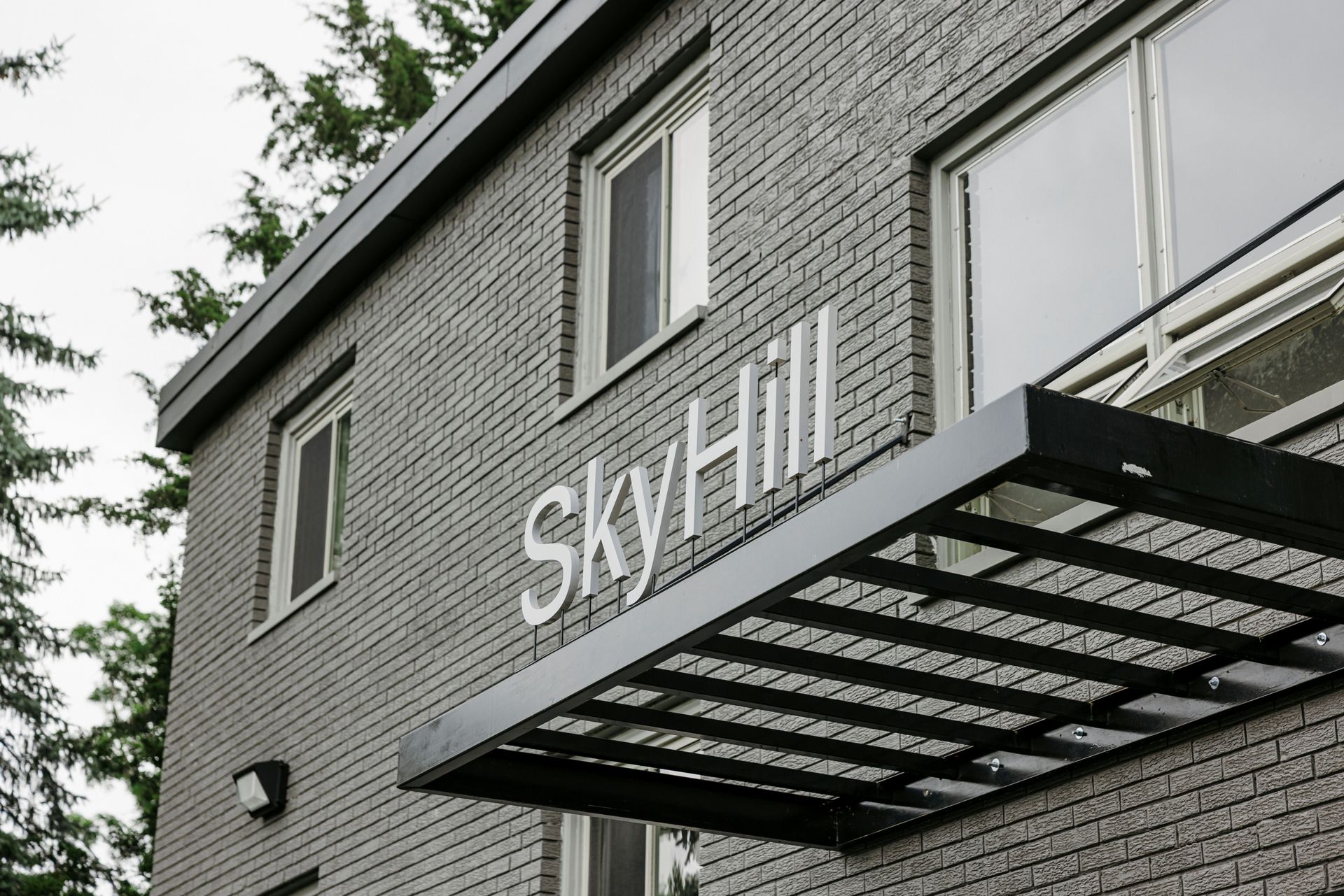 Exterior of gray brick building with “skyhill” sign and metal awning under cloudy sky