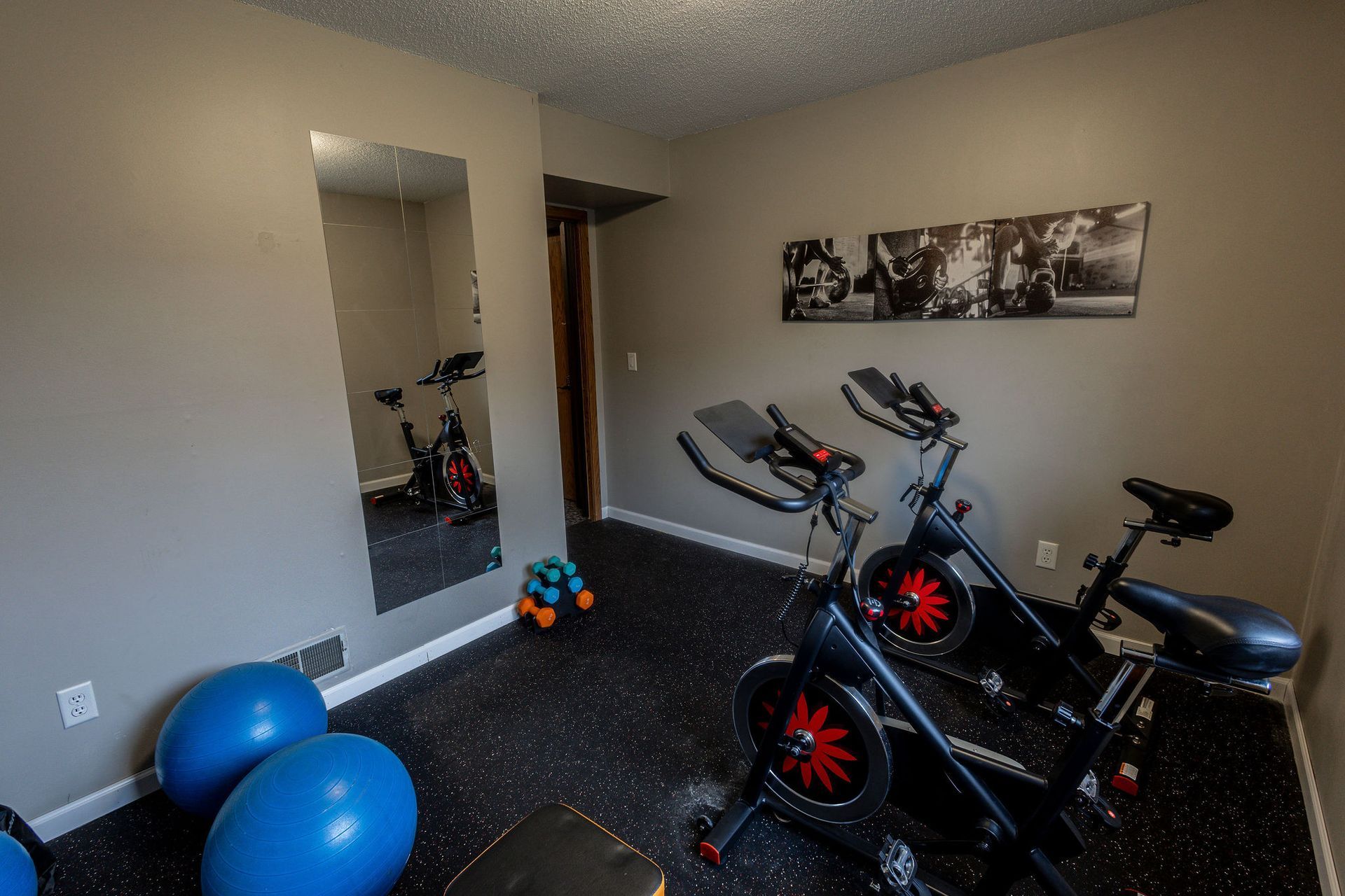 Home exercise room with two stationary bikes, blue exercise balls, and a wall mirror.